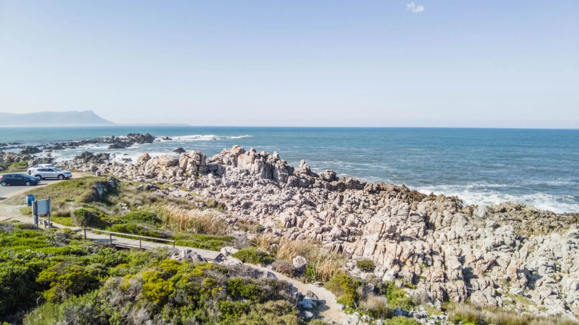 Rocky coastline with a boardwalk and cars parked near the sea.