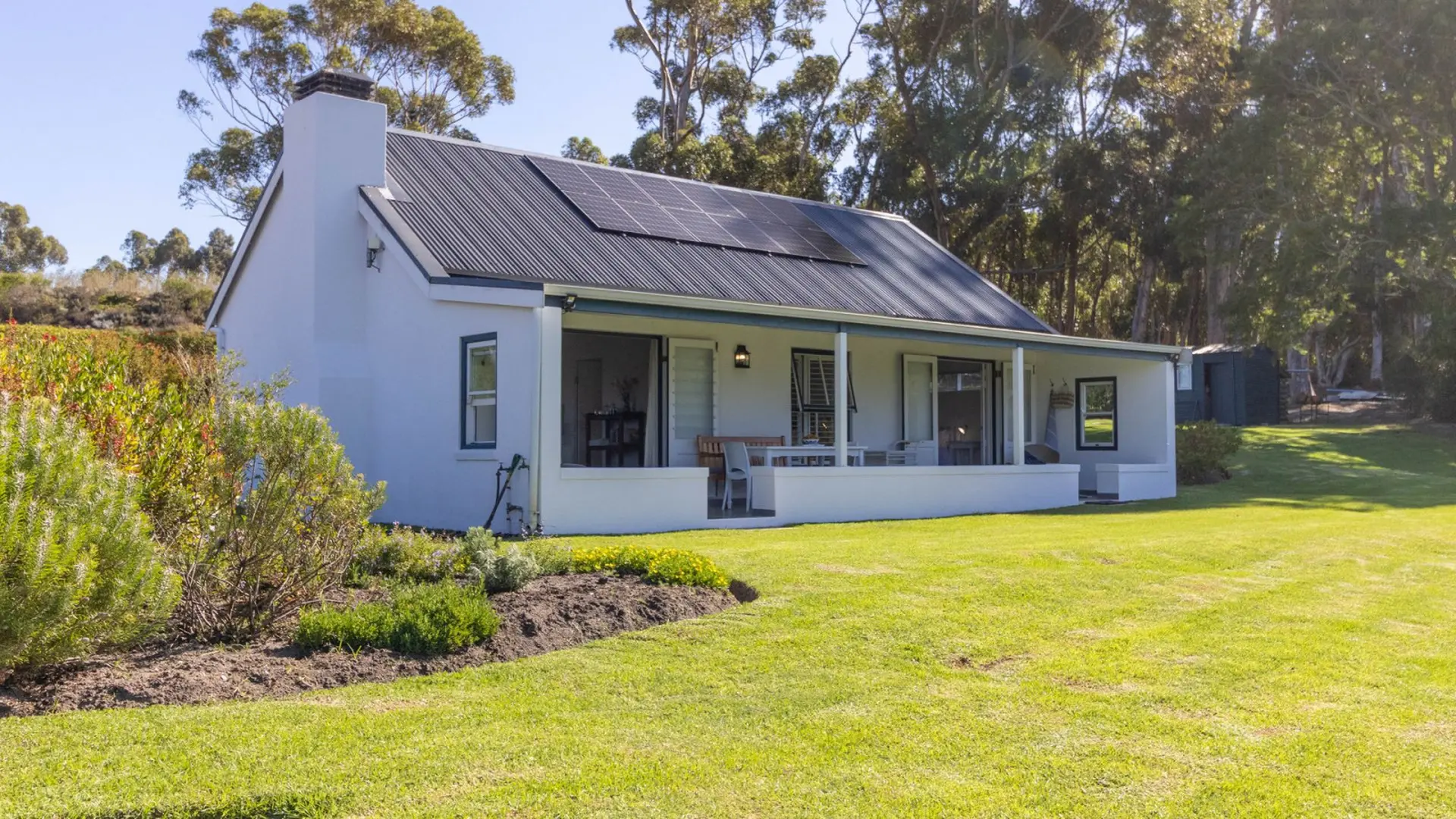 White house with solar panels and a covered patio in a grassy yard.