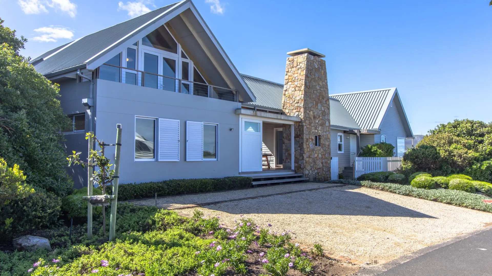 A modern grey house with a stone chimney and a metal roof under a blue sky.