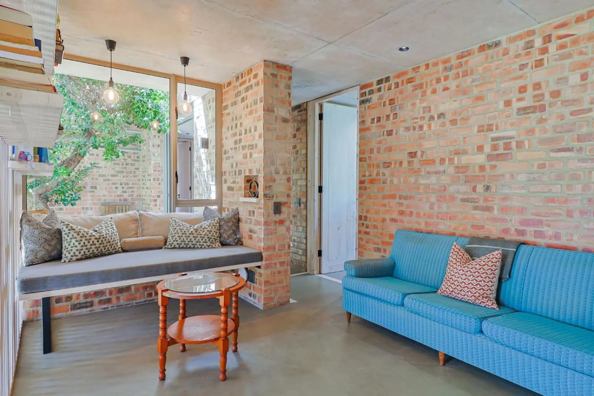 A sun-drenched room with exposed brick walls, a built-in couch, and a blue sofa.