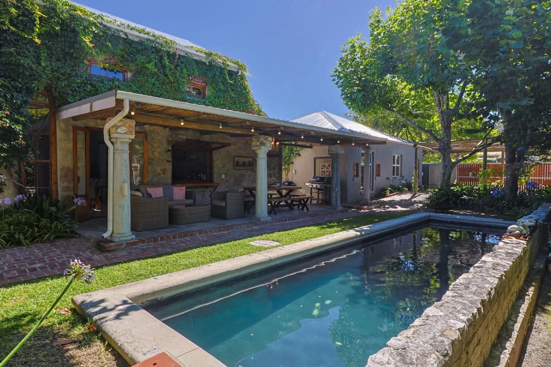 A courtyard with a pool, covered patio, outdoor kitchen, and garden.