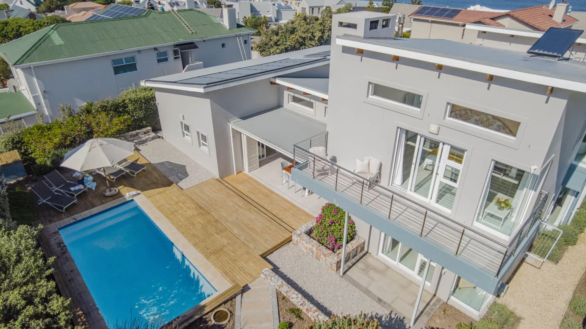 A modern light gray house with a swimming pool and lounge chairs on a wooden deck.