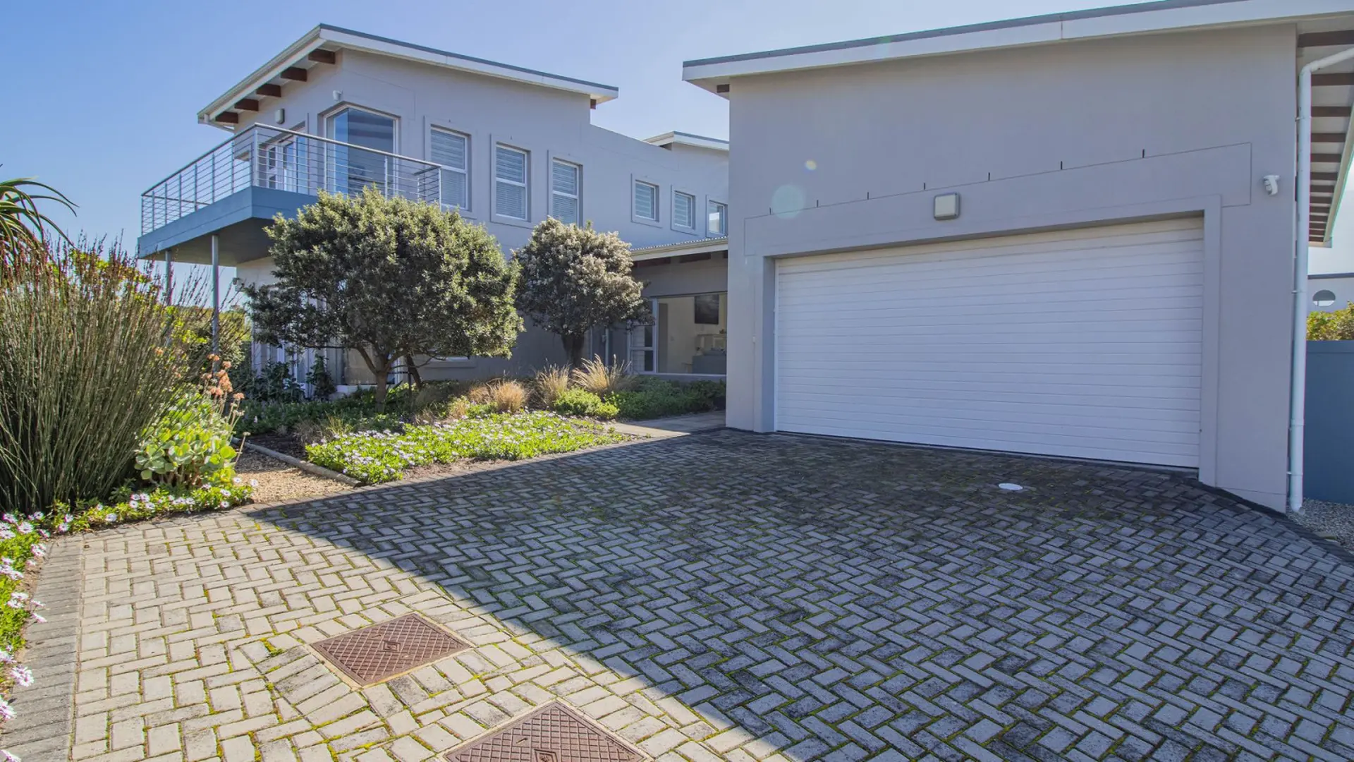 Modern grey house with a large white garage door and a balcony with a metal railing.