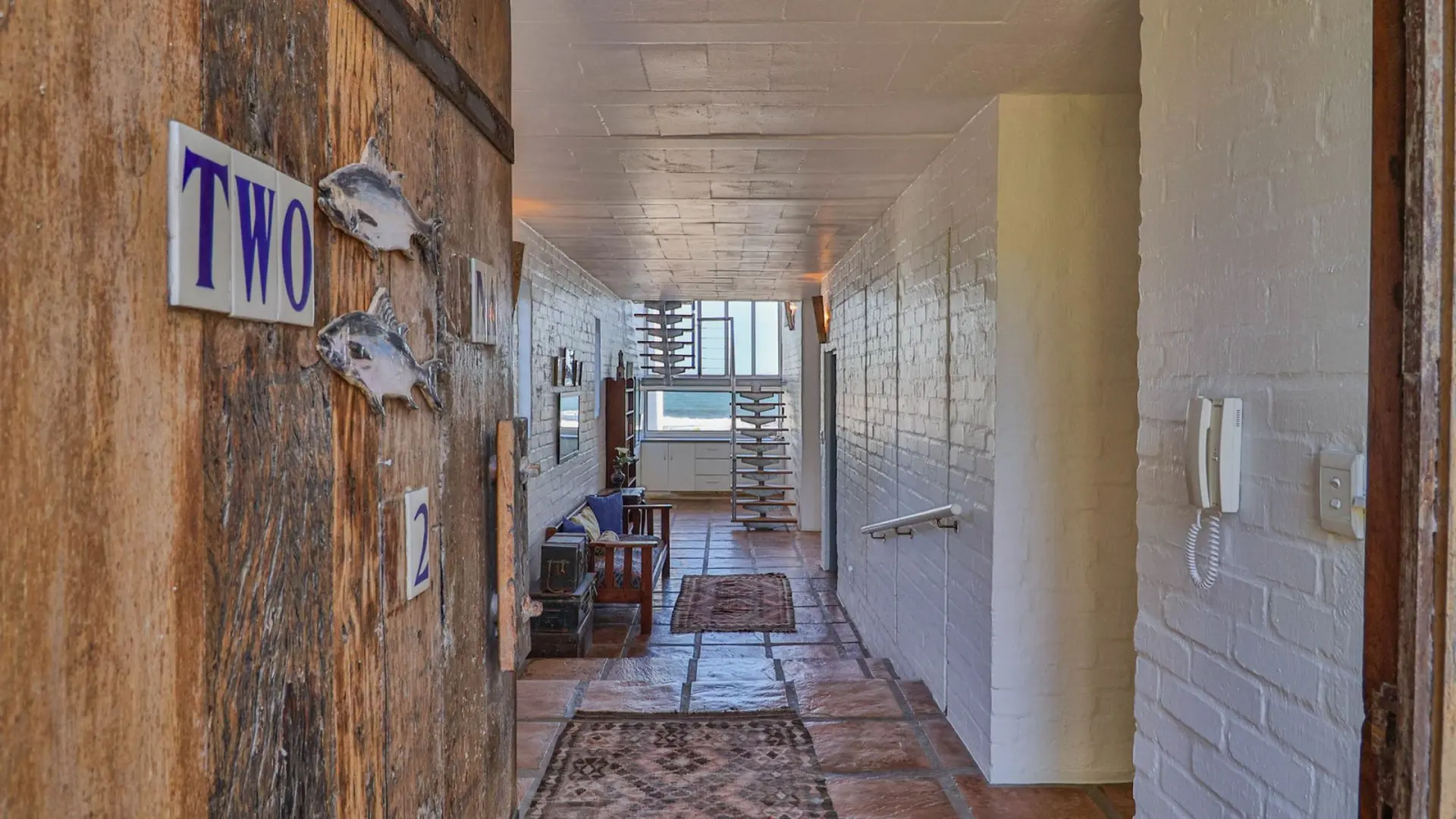Hallway entrance with wooden door and fish art, brick walls, and stairs.