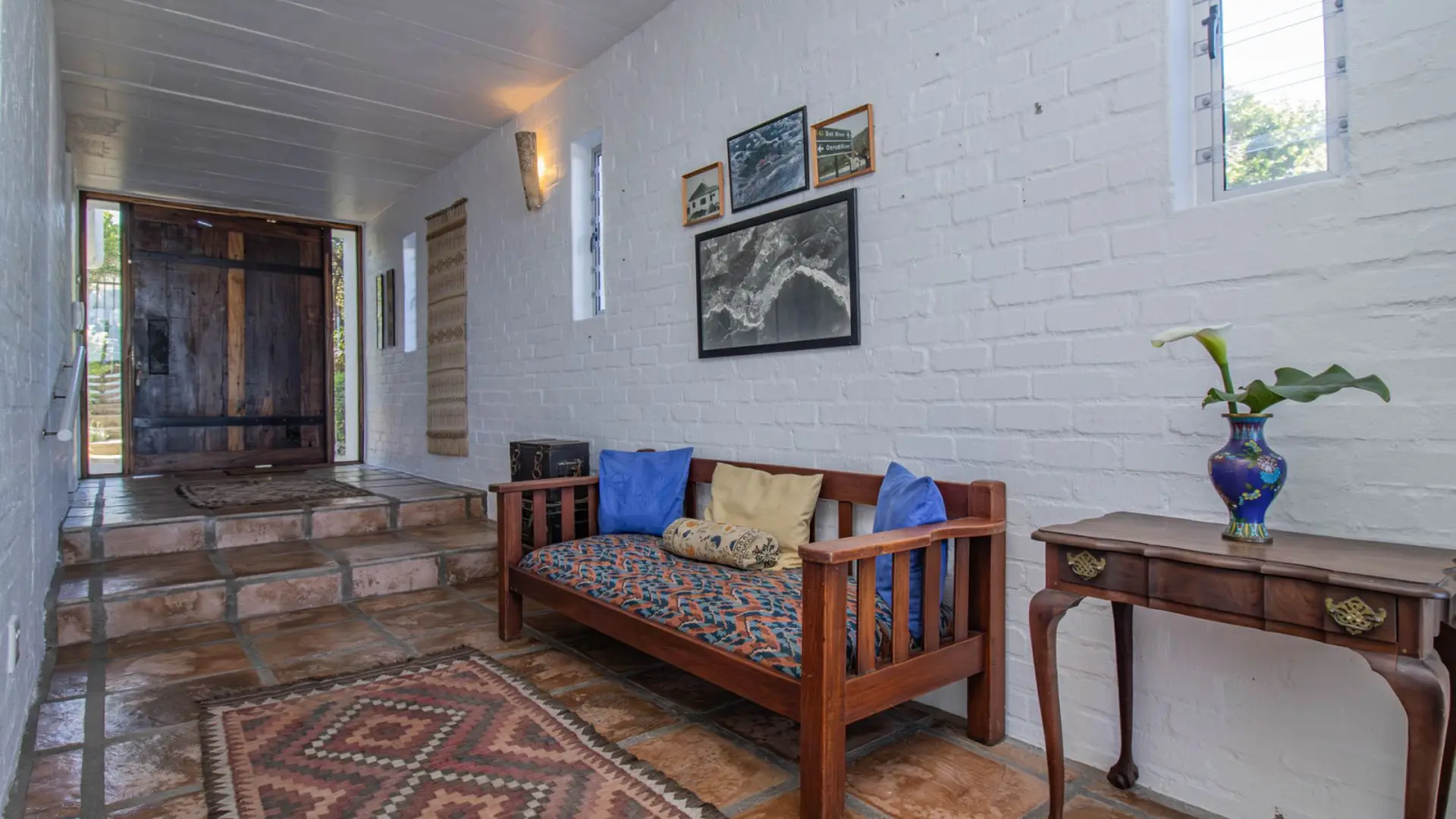 Wooden furniture, white brick walls, and tiled floors in a hallway with a large wooden door.