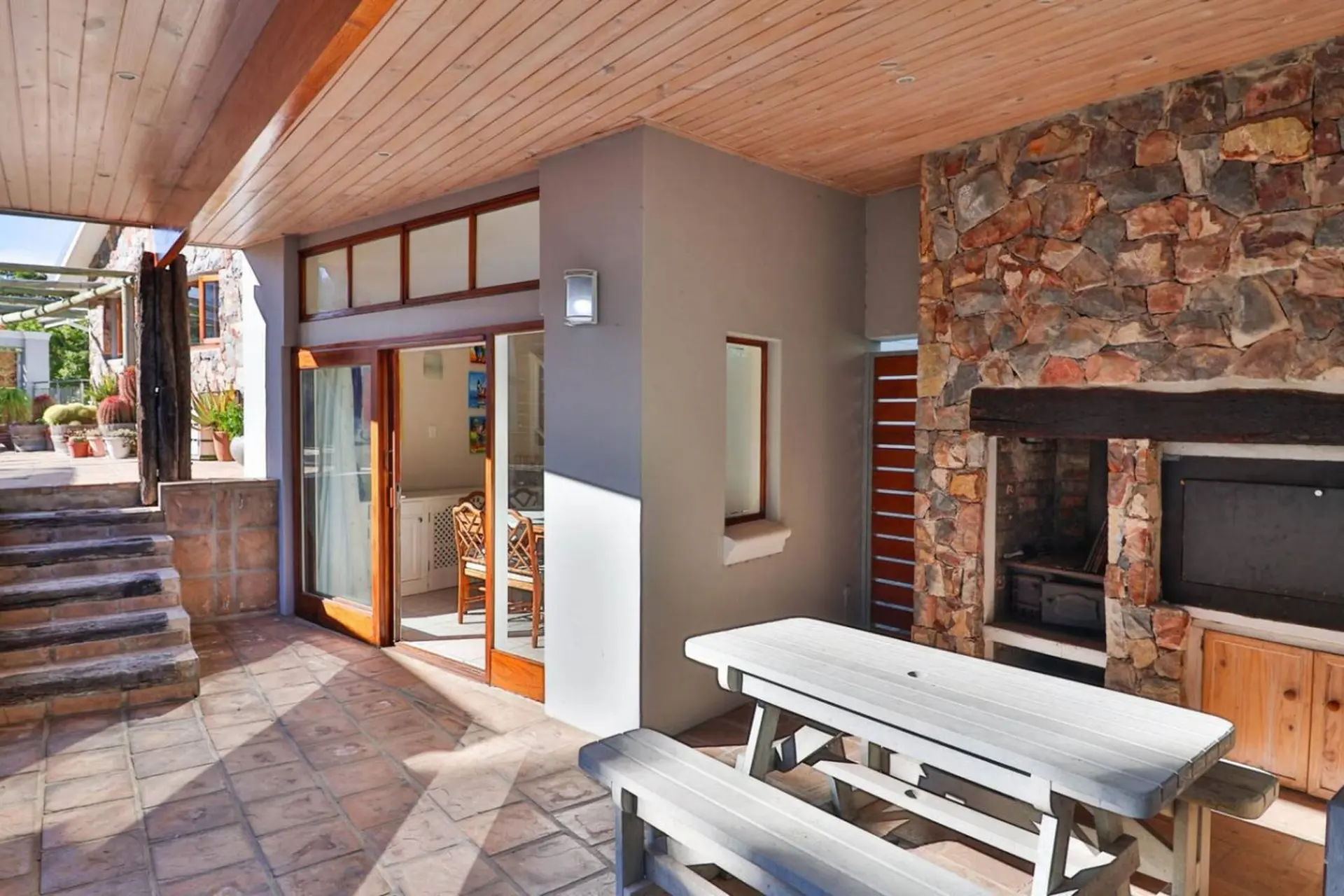 A covered patio with a stone fireplace, picnic table, and outdoor seating.