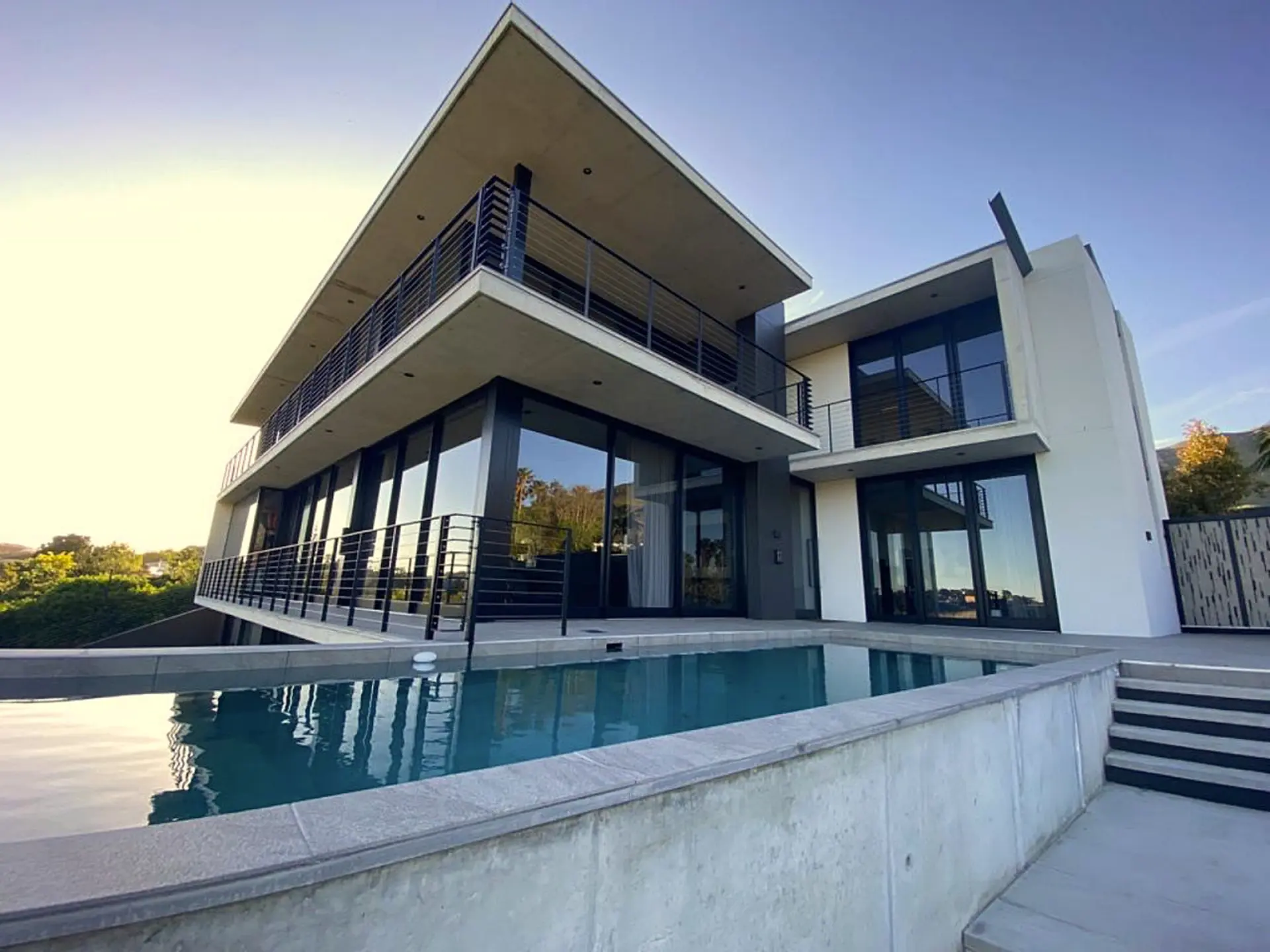Modern house with a swimming pool and balconies, set against a clear blue sky.