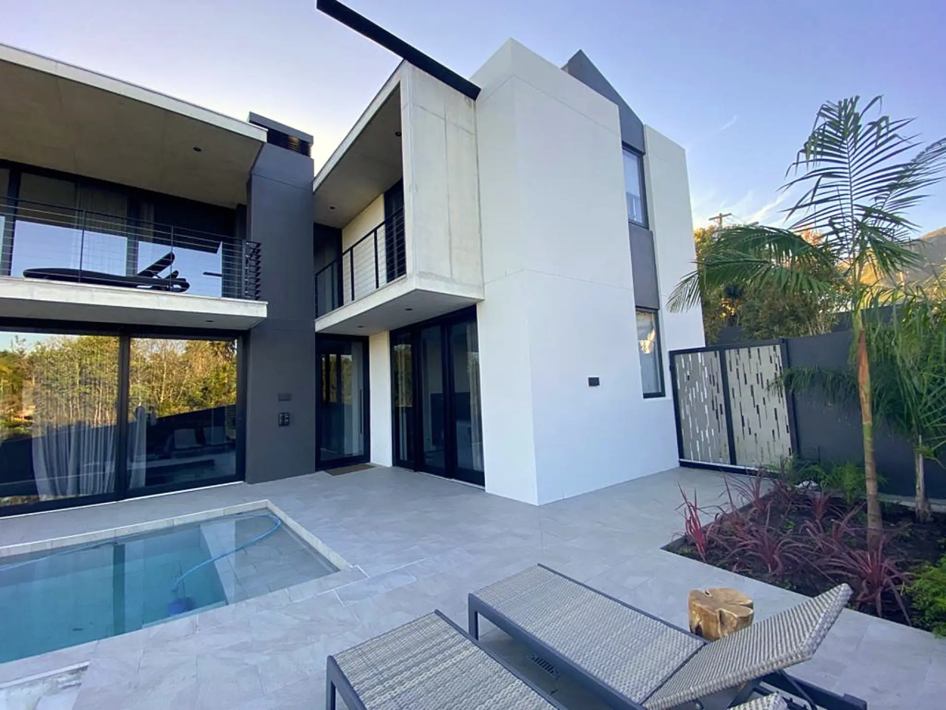 Modern house with a pool, lounge chairs, and palm trees.