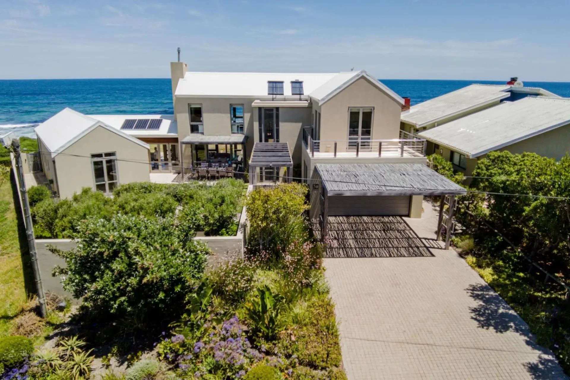 Modern beach house with a white roof and large windows overlooking the ocean.