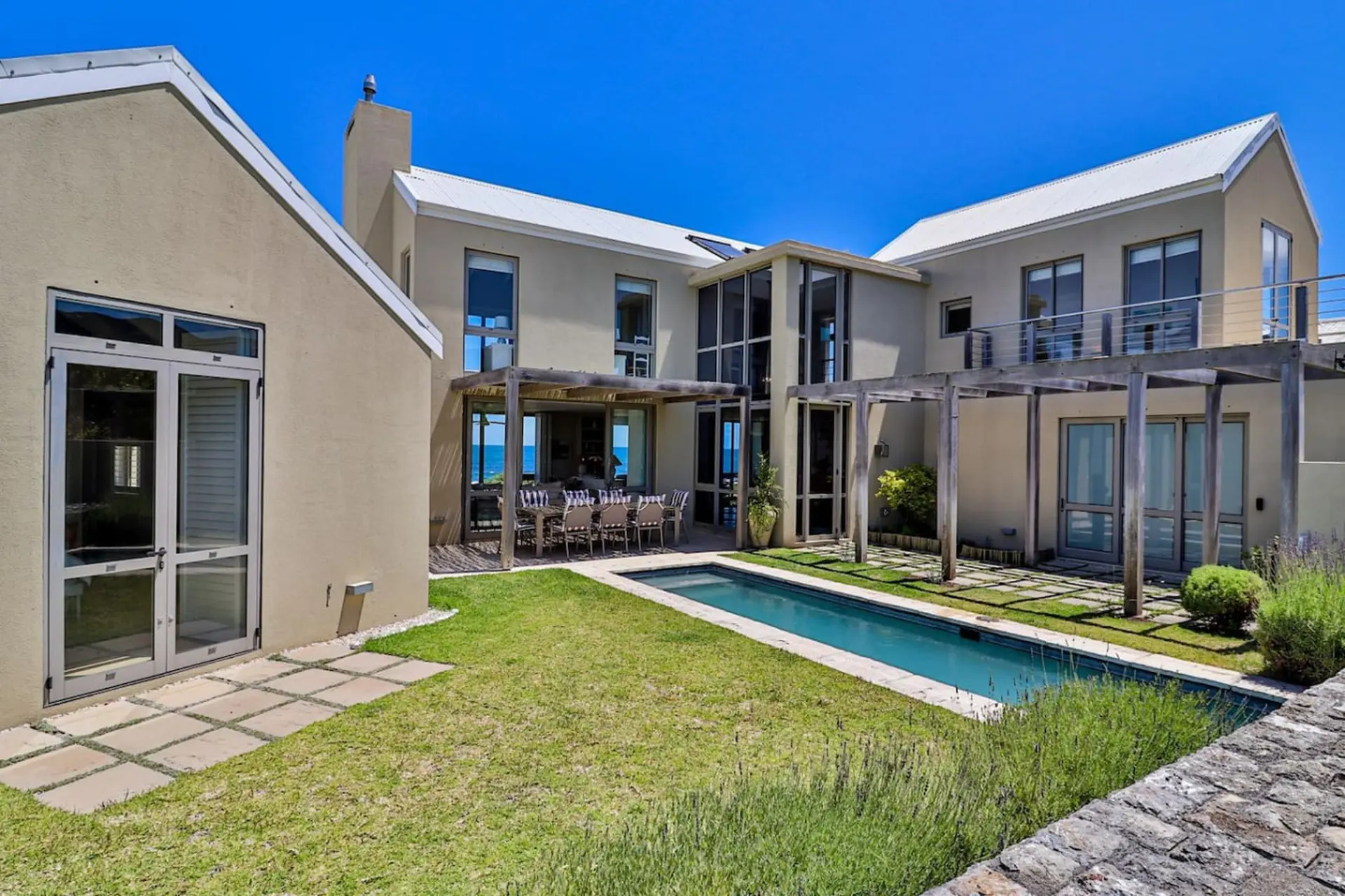 Modern house with a swimming pool and outdoor dining area, overlooking the ocean.