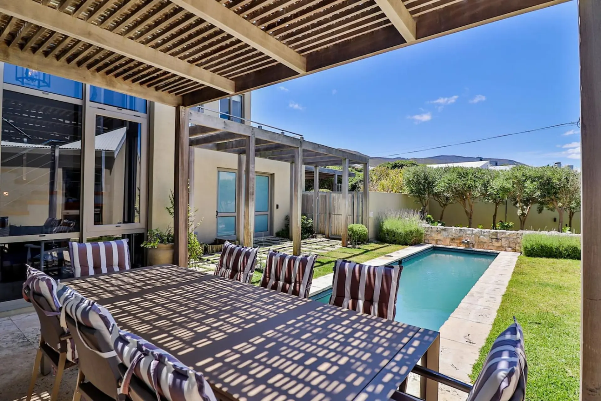 Outdoor dining area with chairs surrounding a table, near a pool and lush greenery.