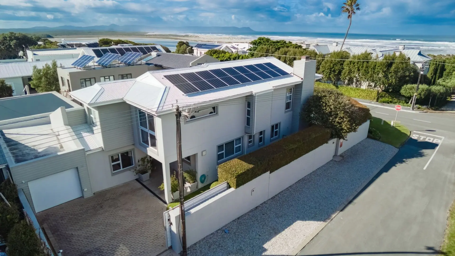 Aerial view of a modern house with solar panels, garage, and a view of the ocean.