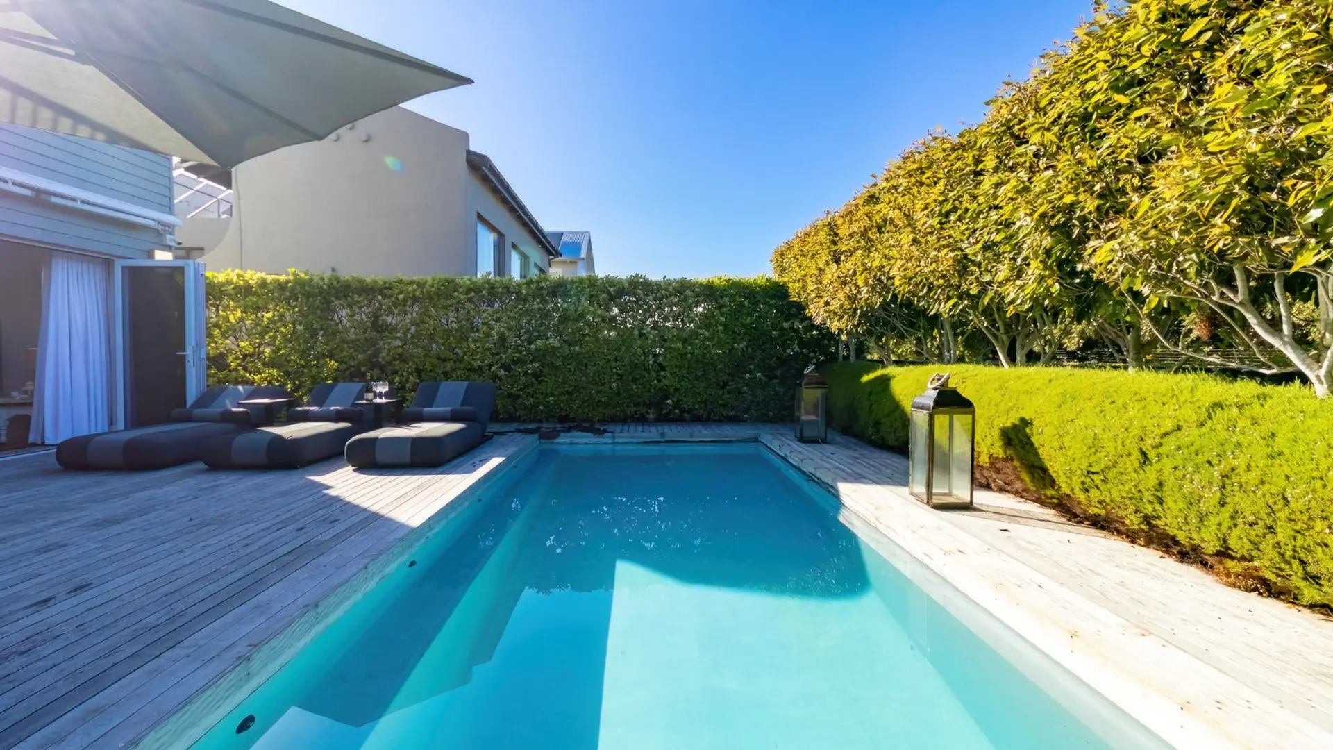 Luxury outdoor pool with lounge chairs and lush greenery under a bright blue sky.