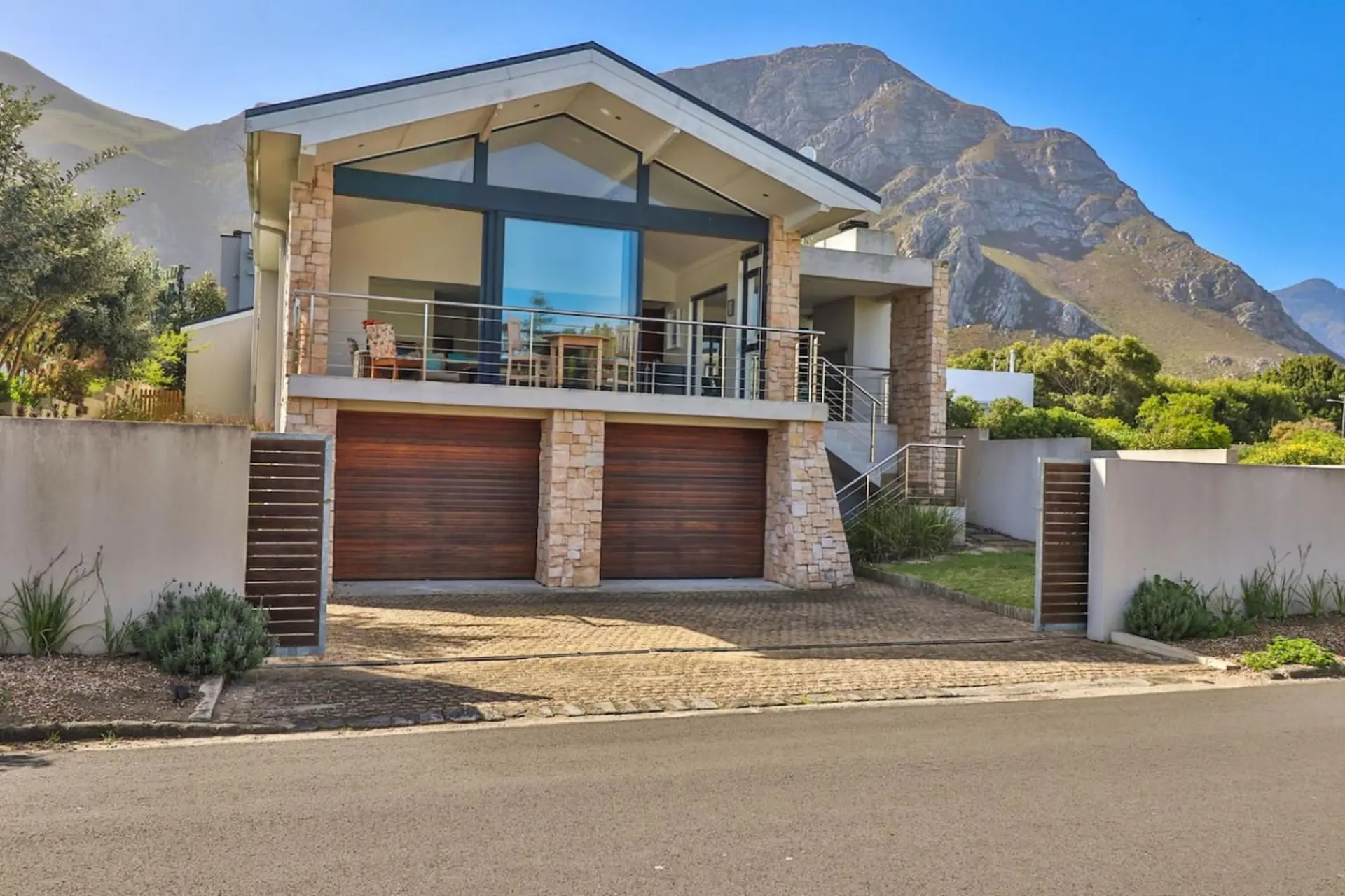 Modern house with stone accents and large windows, facing a mountain landscape.