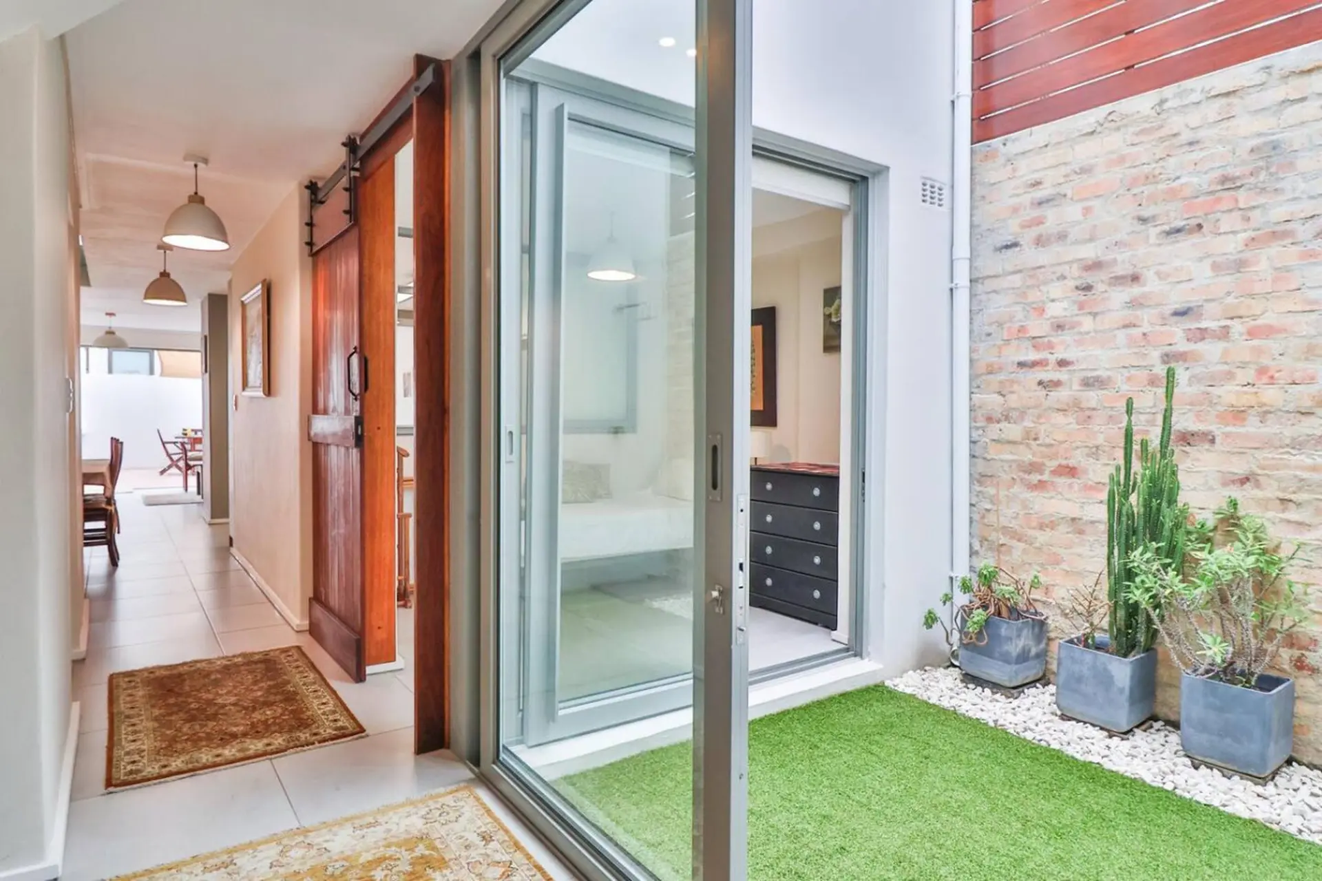 A hallway leads to an open doorway revealing a bedroom, with a courtyard garden to the right.