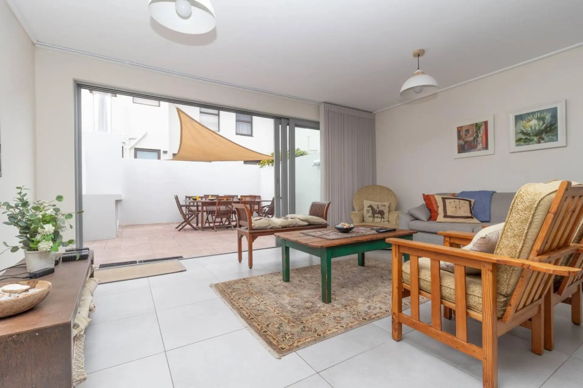 Living room with a sofa, chairs, and coffee table, opening to an outdoor patio with a dining set.
