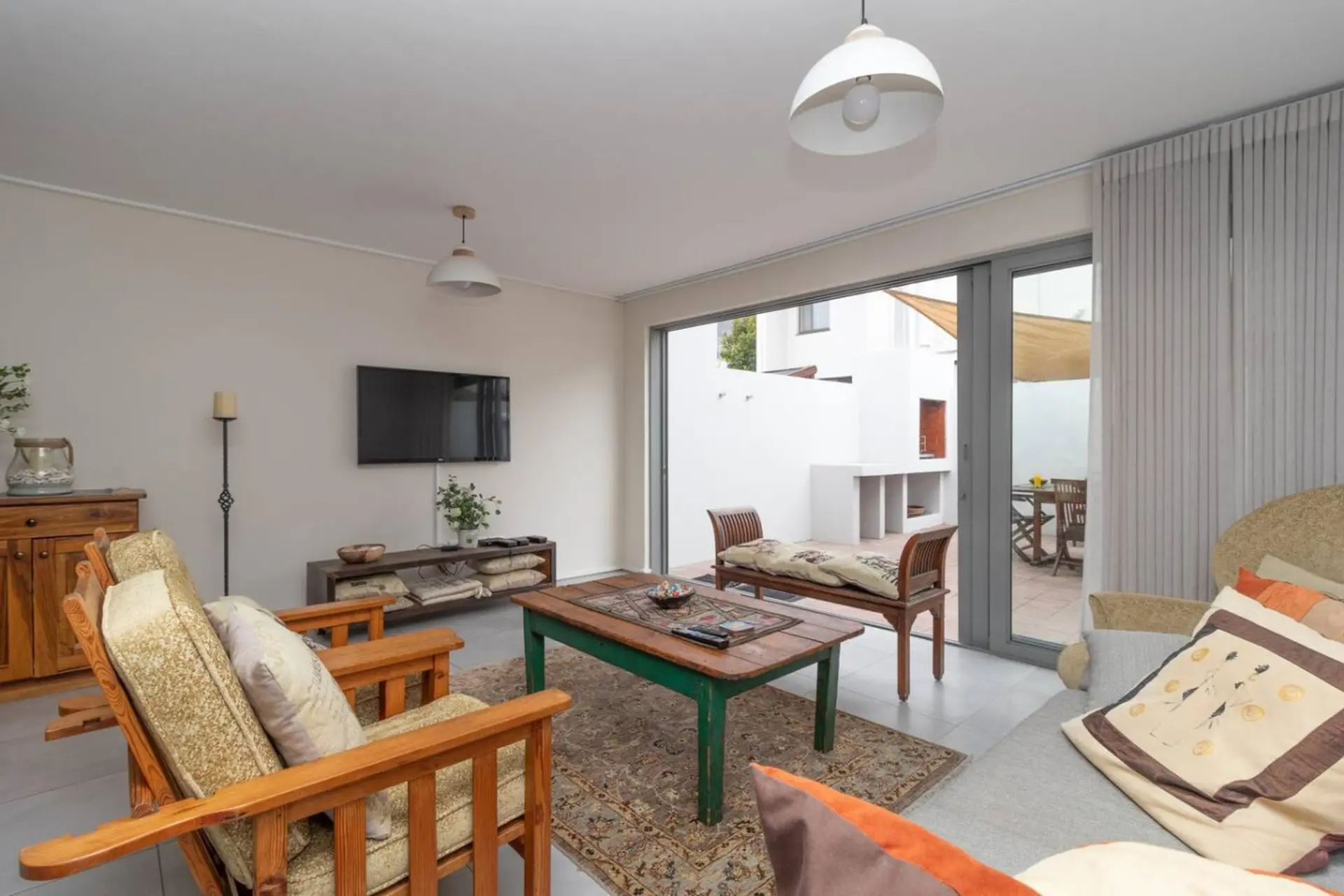 A modern living room with wooden furniture, a TV, and a large sliding glass door leading to a patio.