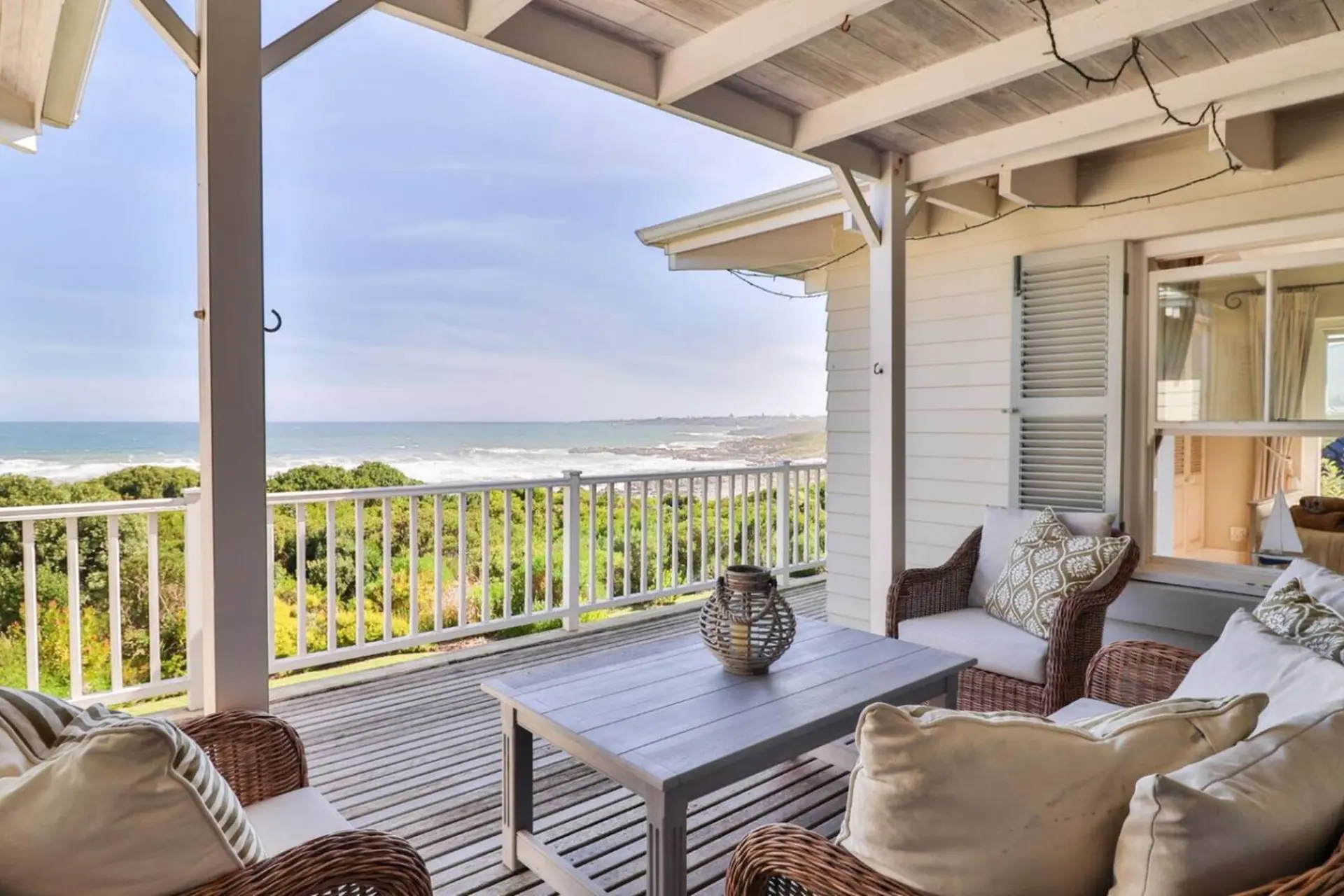 A covered patio with wicker furniture overlooks the ocean and a white railing.