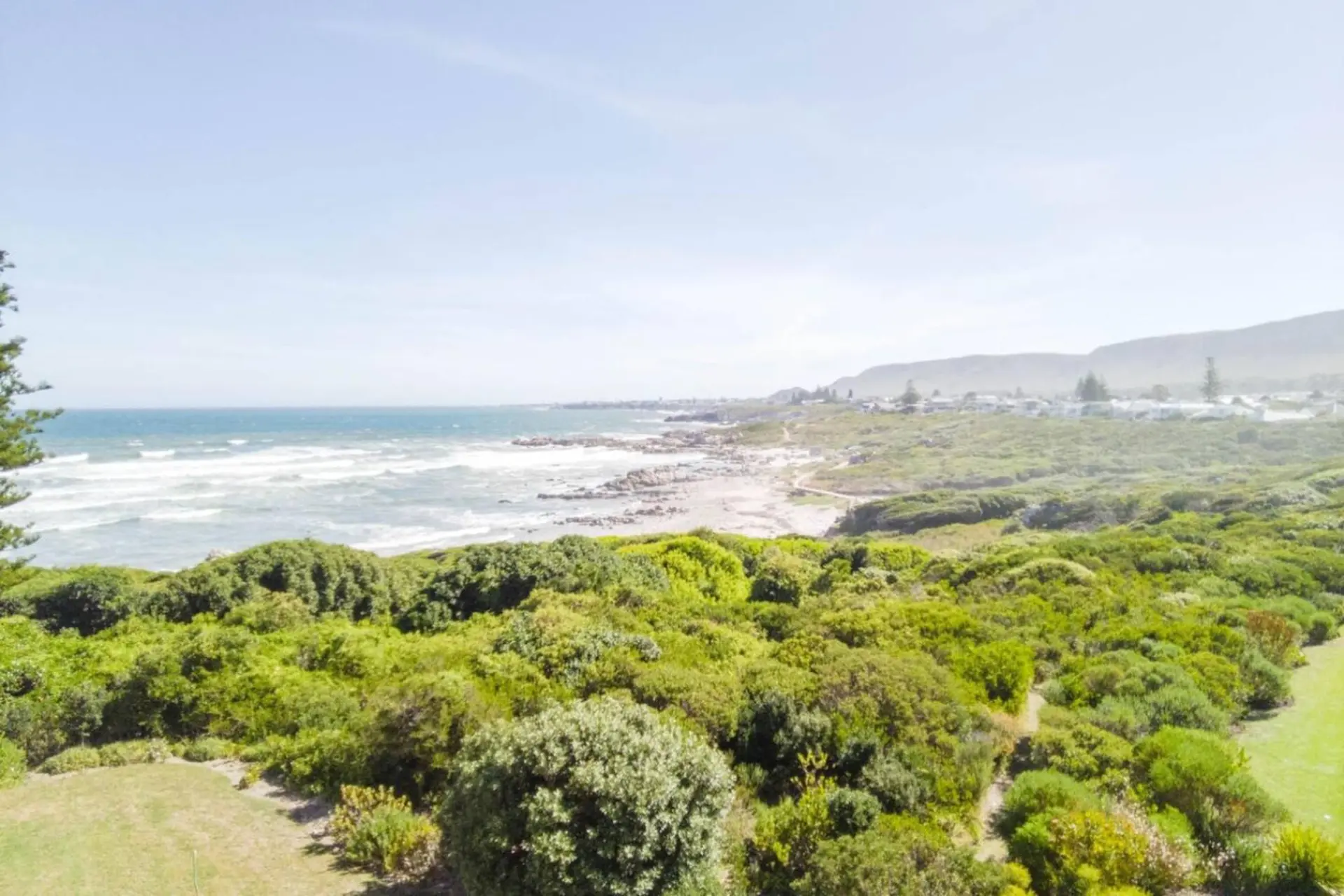A coastal view with a sandy beach, choppy blue ocean waves, and a small town in the distance.
