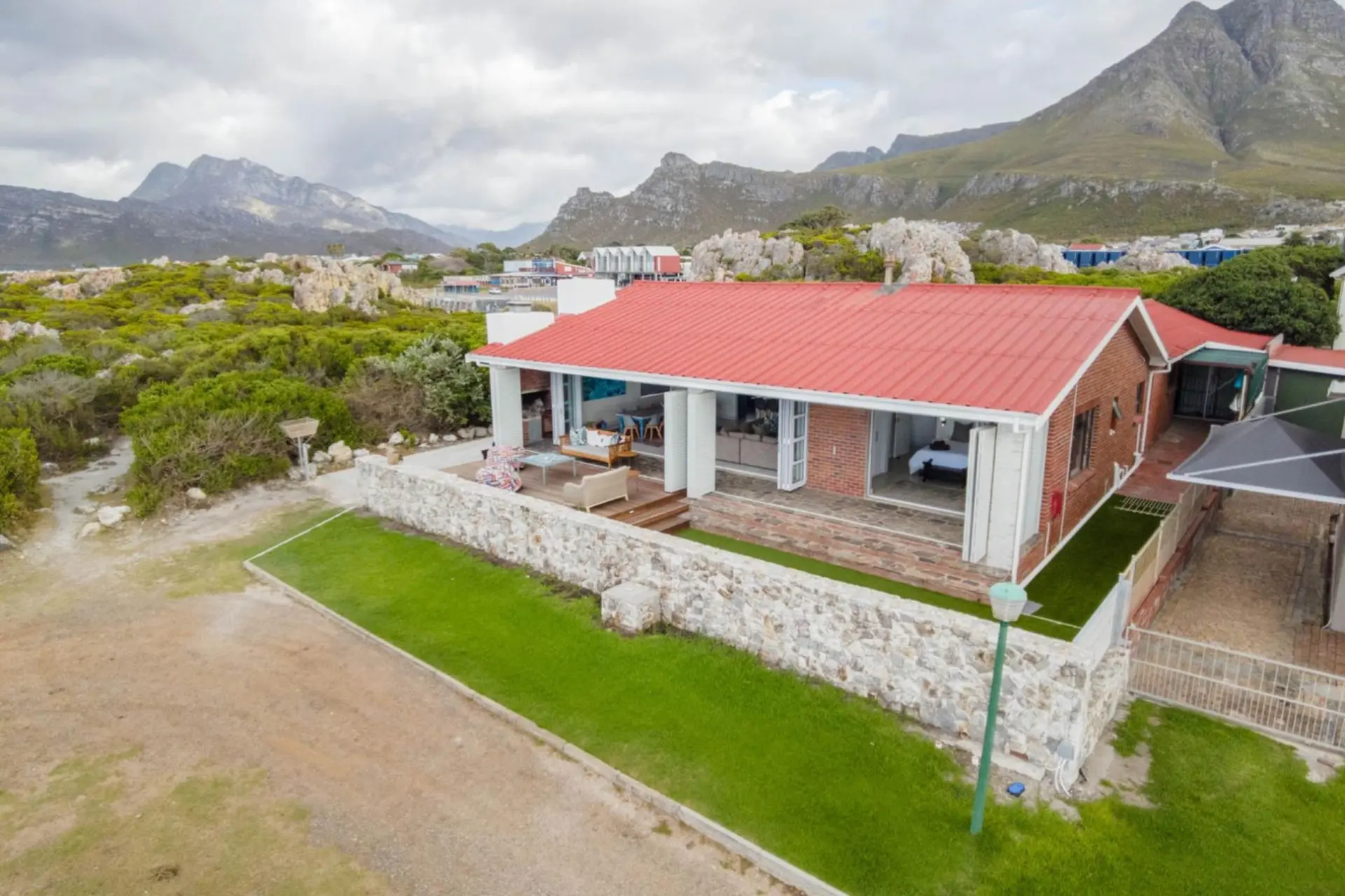 Modern house with red roof and brick exterior, overlooking mountains and lush greenery.