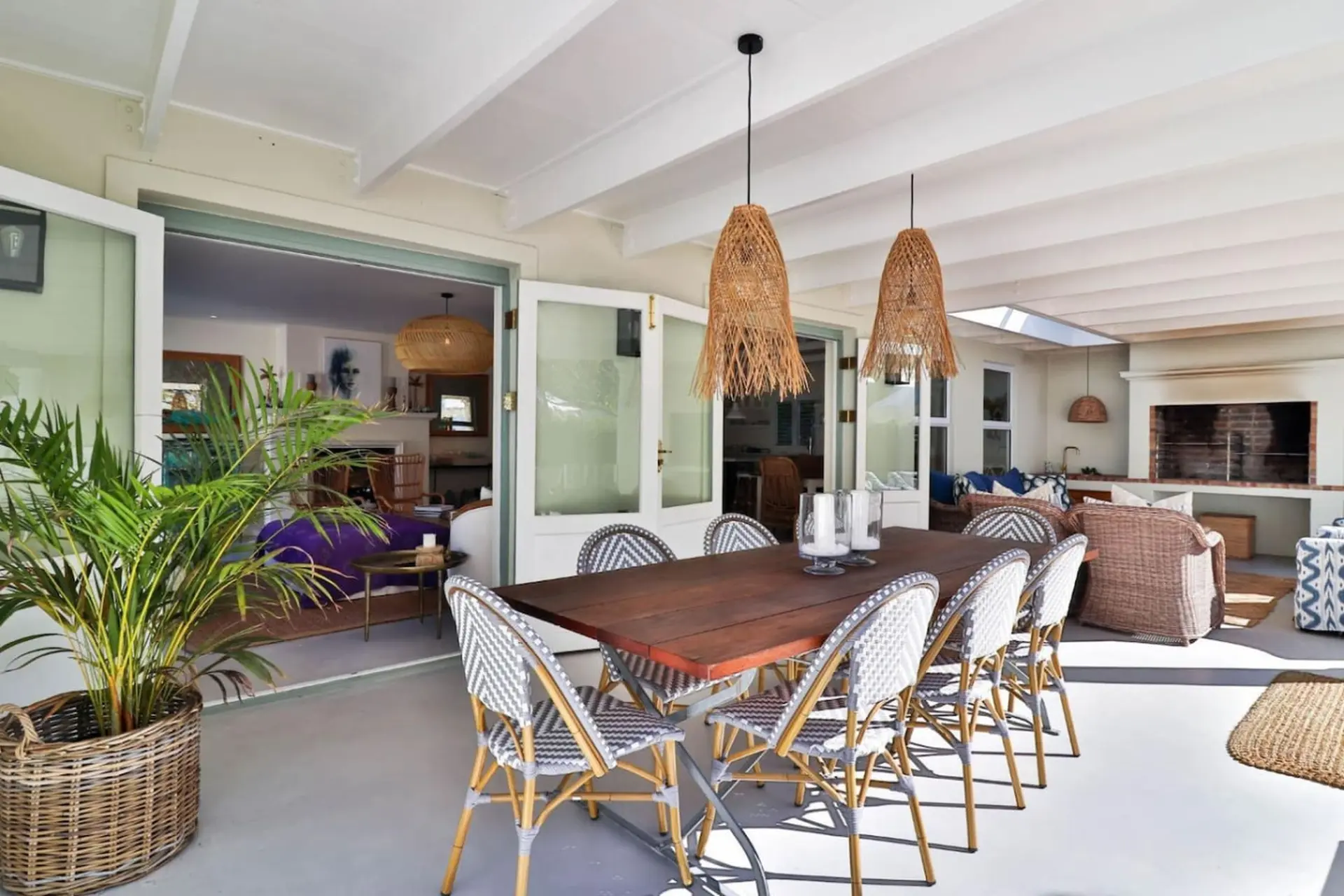 An outdoor dining area with a wooden table and chairs, overlooking an indoor living space.