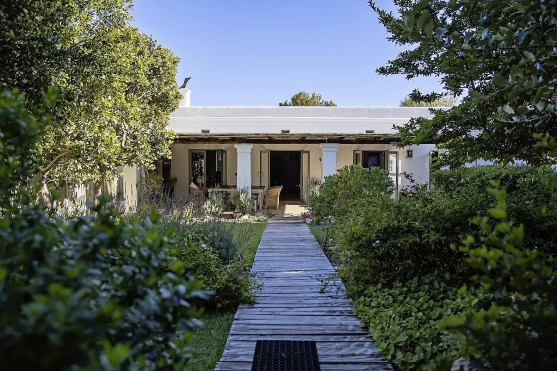 A weathered wooden walkway leads to a white, single-story home with a porch and columns.