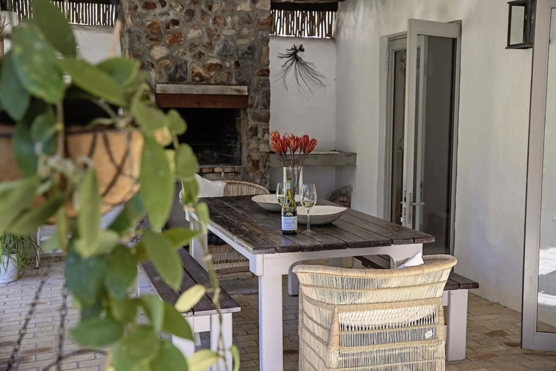 A dining table set on a patio with chairs, a fireplace, and plants.