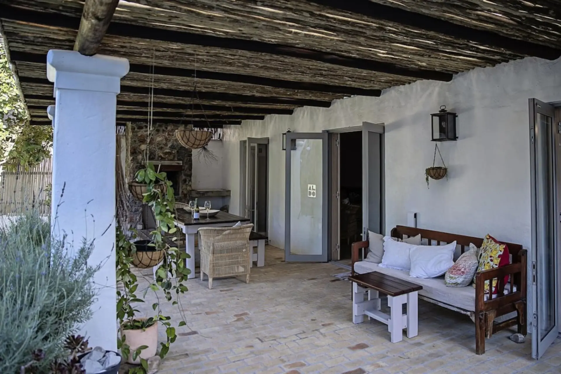 A rustic patio with a wooden bench, wicker chairs, and hanging plants.