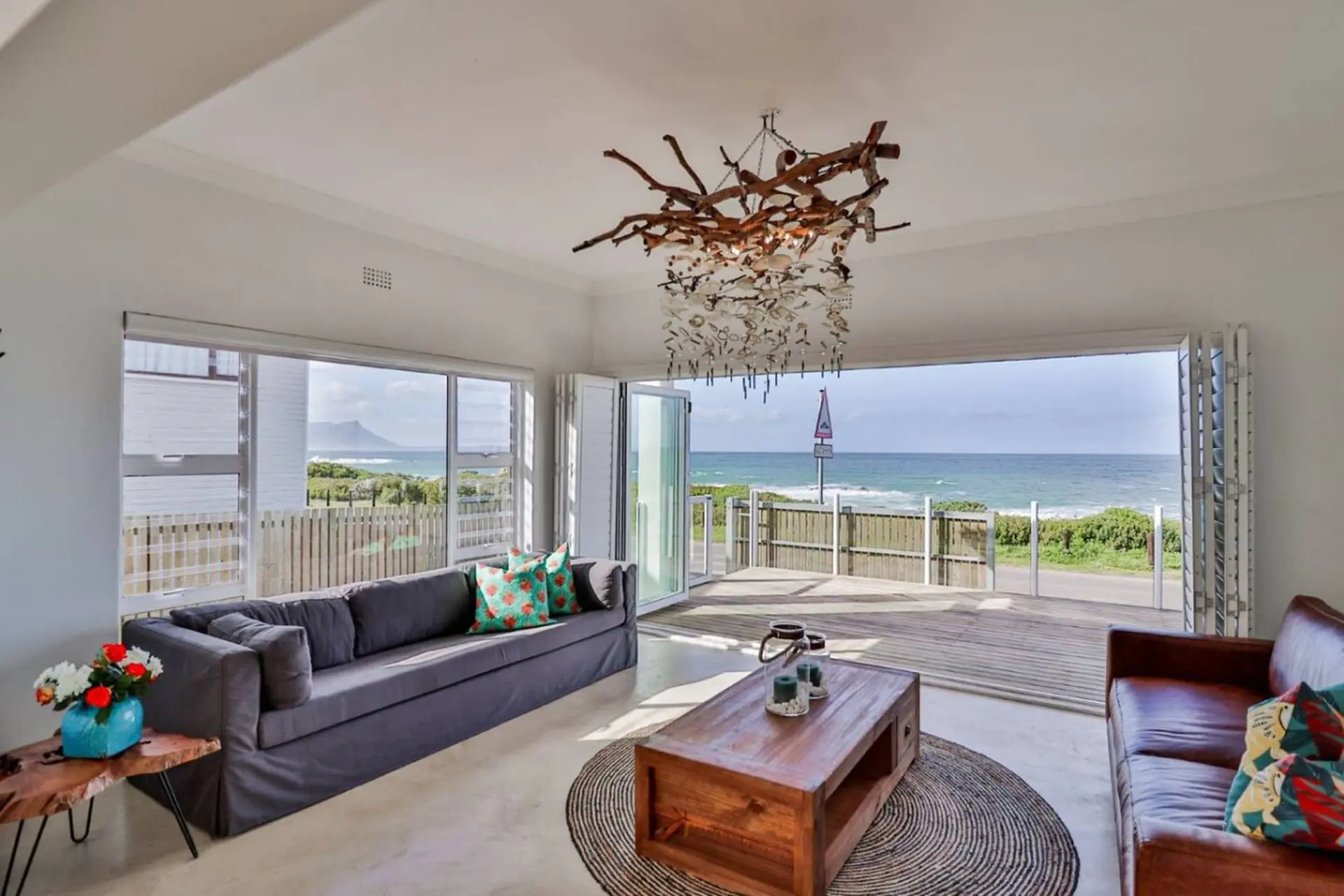 A chic living room with a grey couch facing a wooden coffee table and a view of the ocean.