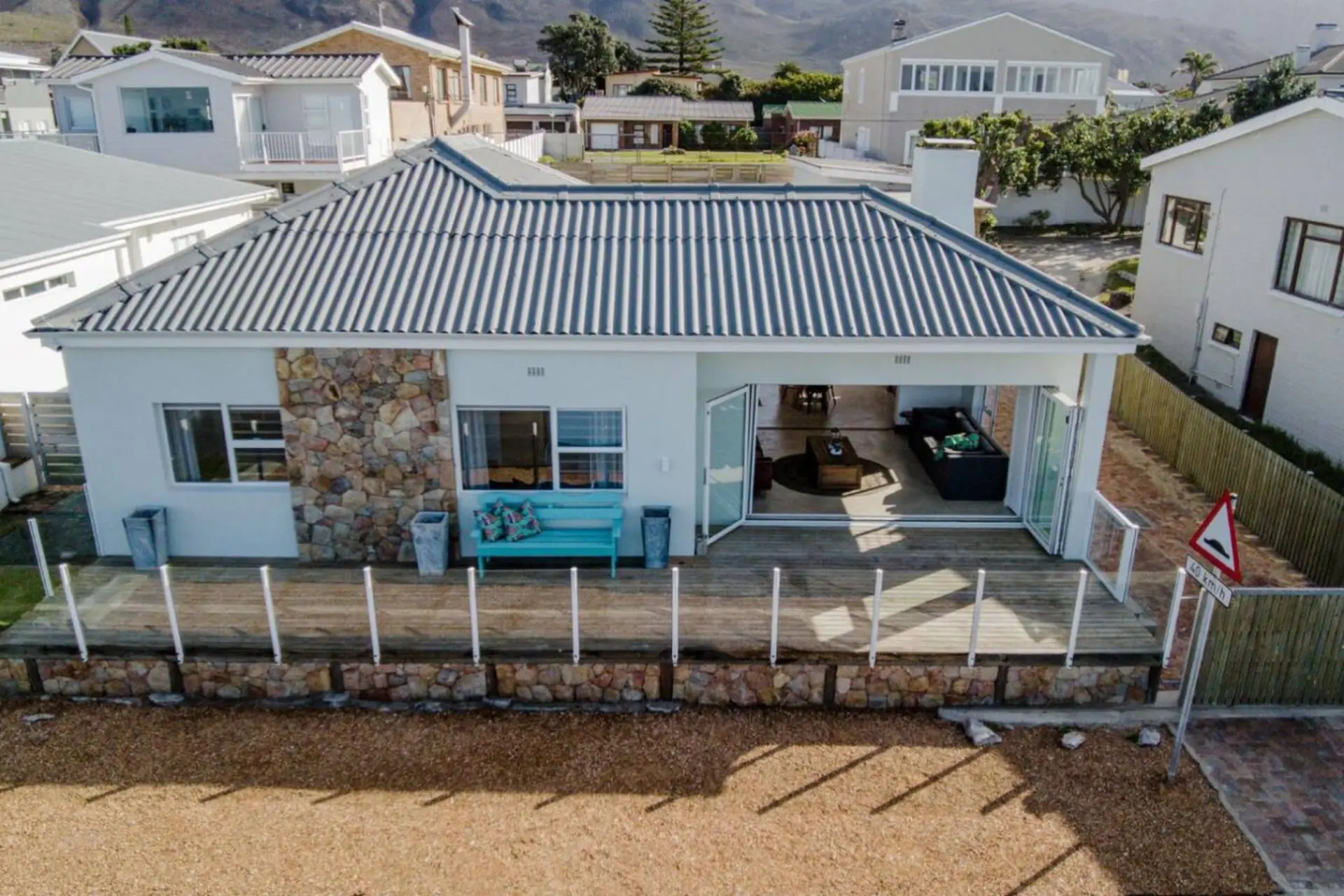 A light blue house with a gray roof and stone accent wall sits on a deck.