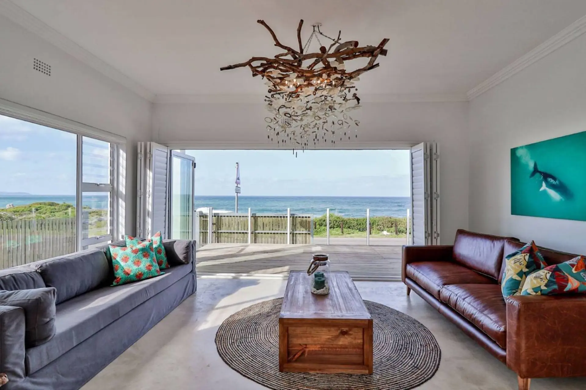 Living room with beach view, featuring a gray sofa, brown leather sofa, coffee table, and artwork of