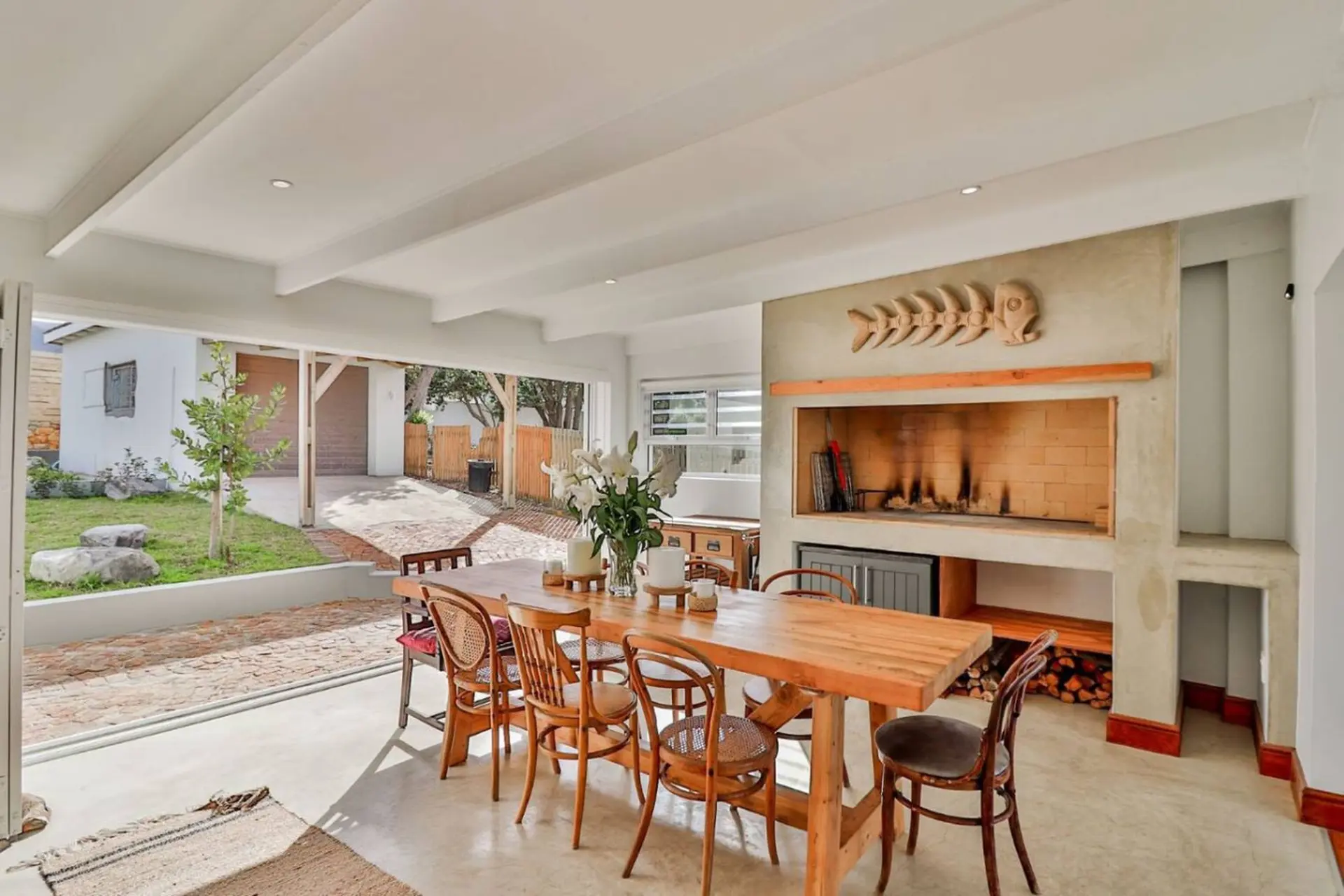 A wooden dining table with chairs is set in front of a large fireplace.
