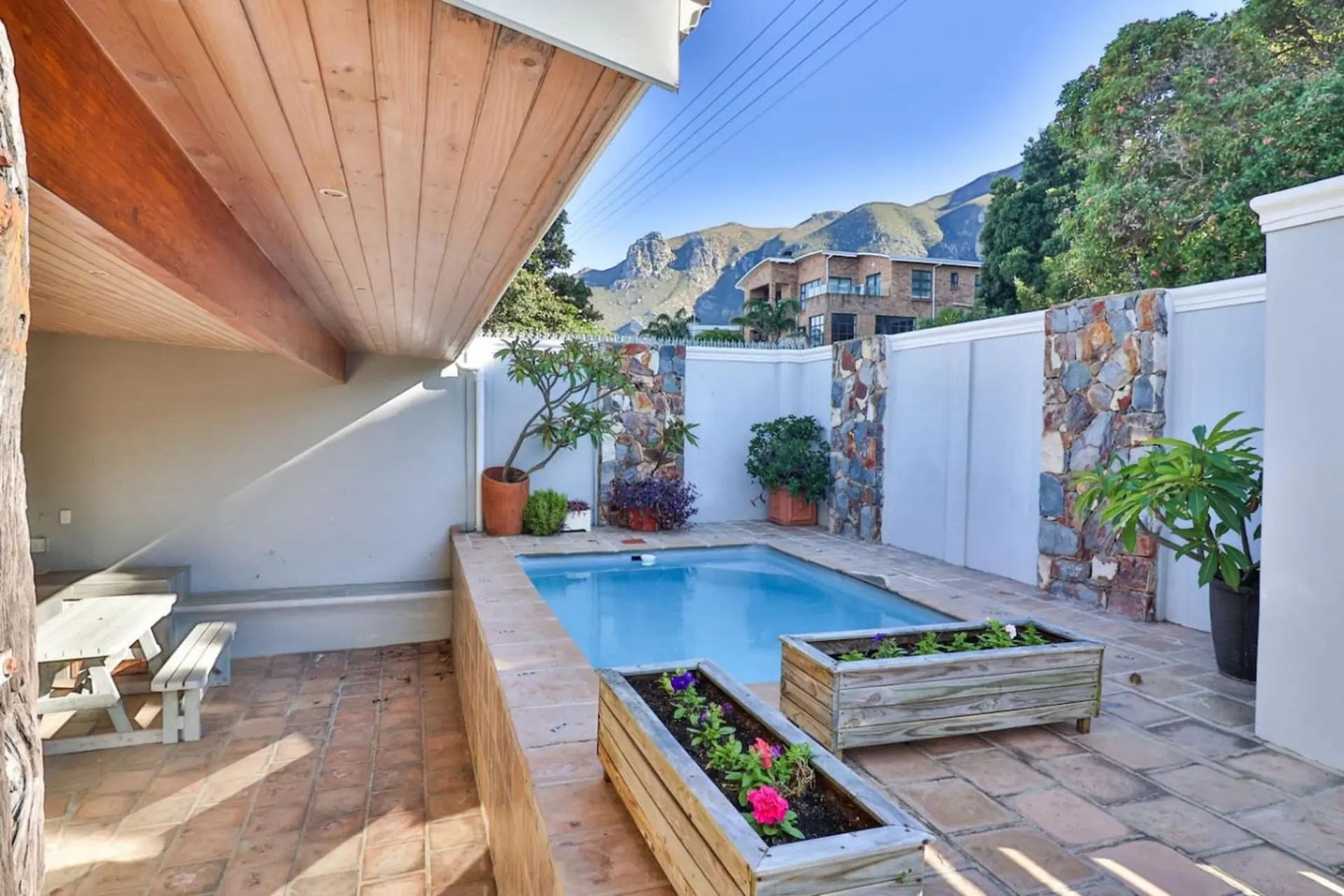A courtyard pool with a picnic table and colorful flowers, backed by mountains.
