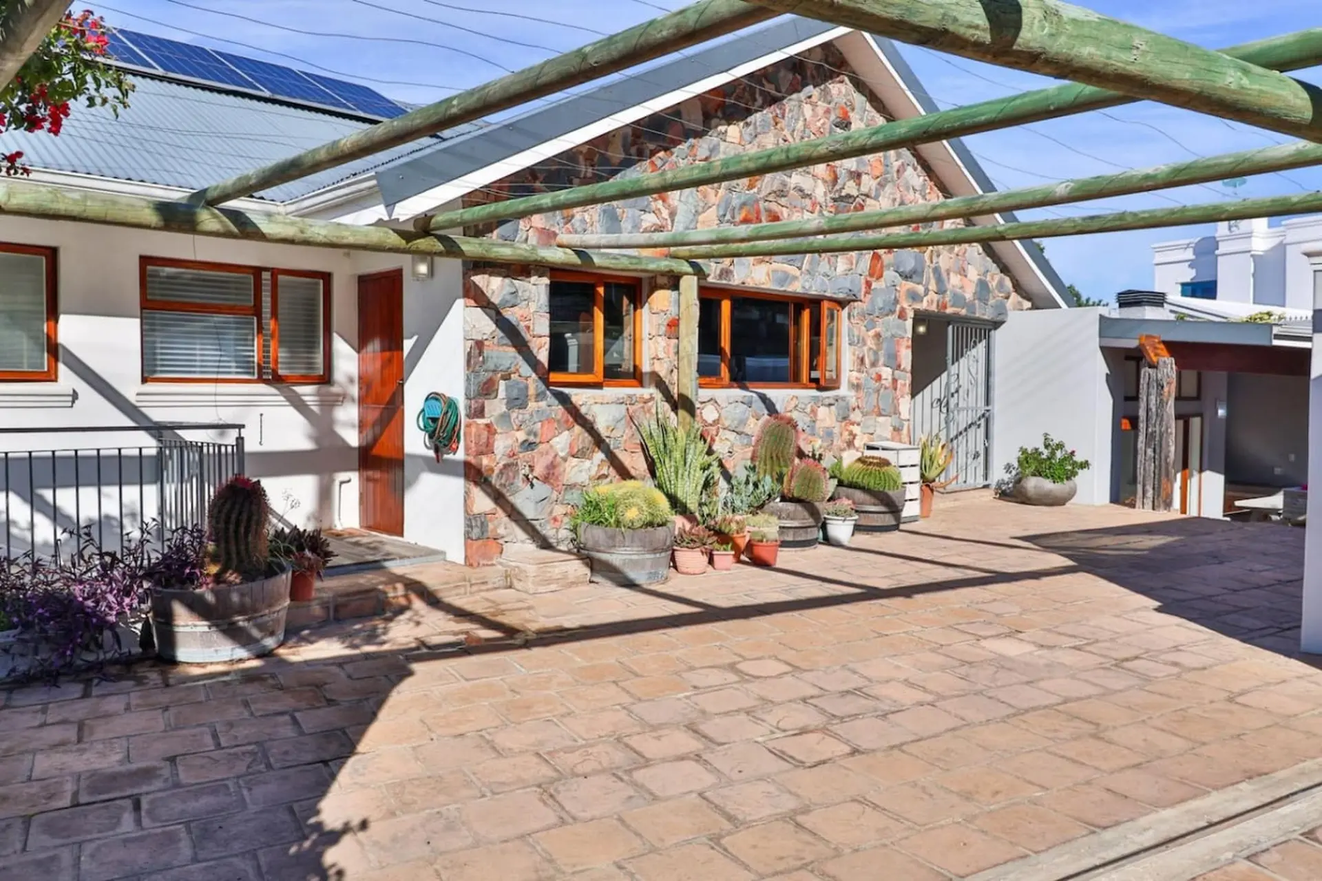 A sunny patio with various succulents and cacti in pots outside a stone house.