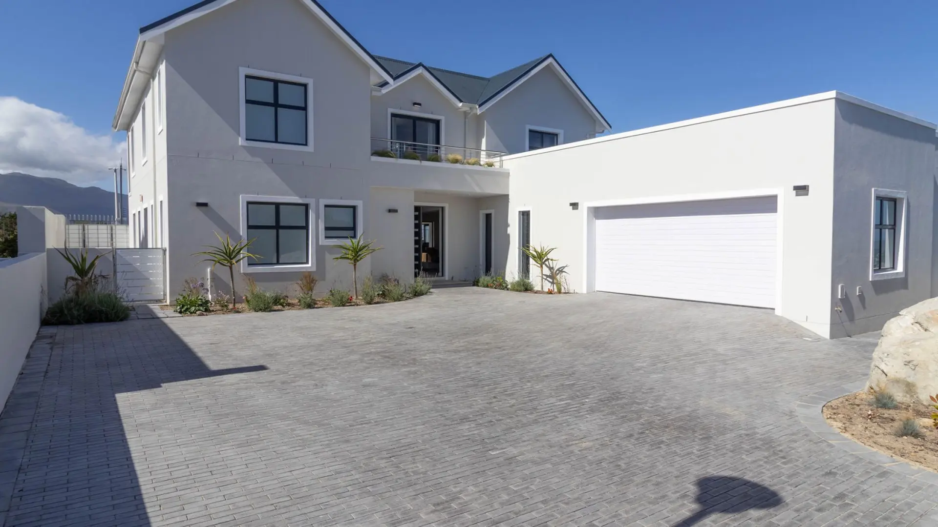 Modern house with grey brick driveway and white garage door.