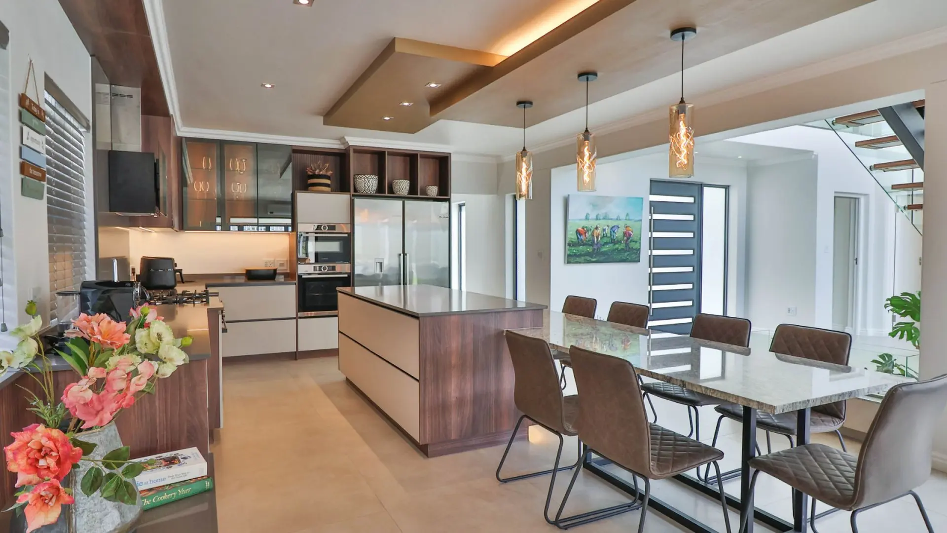 Modern kitchen and dining area with island, refrigerator, oven, dining table and chairs.