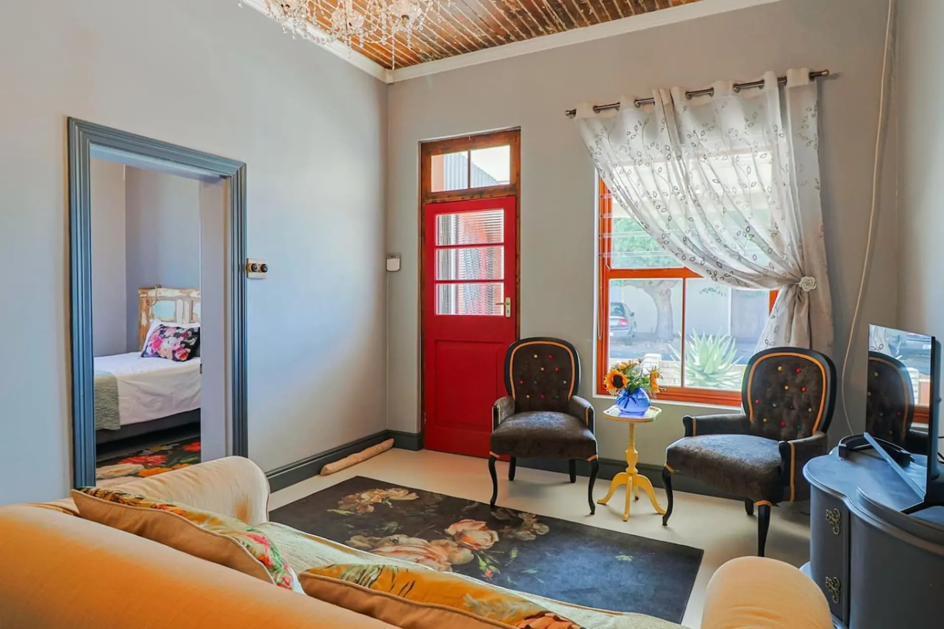 A cozy living room with a red door, two chairs, and a couch.