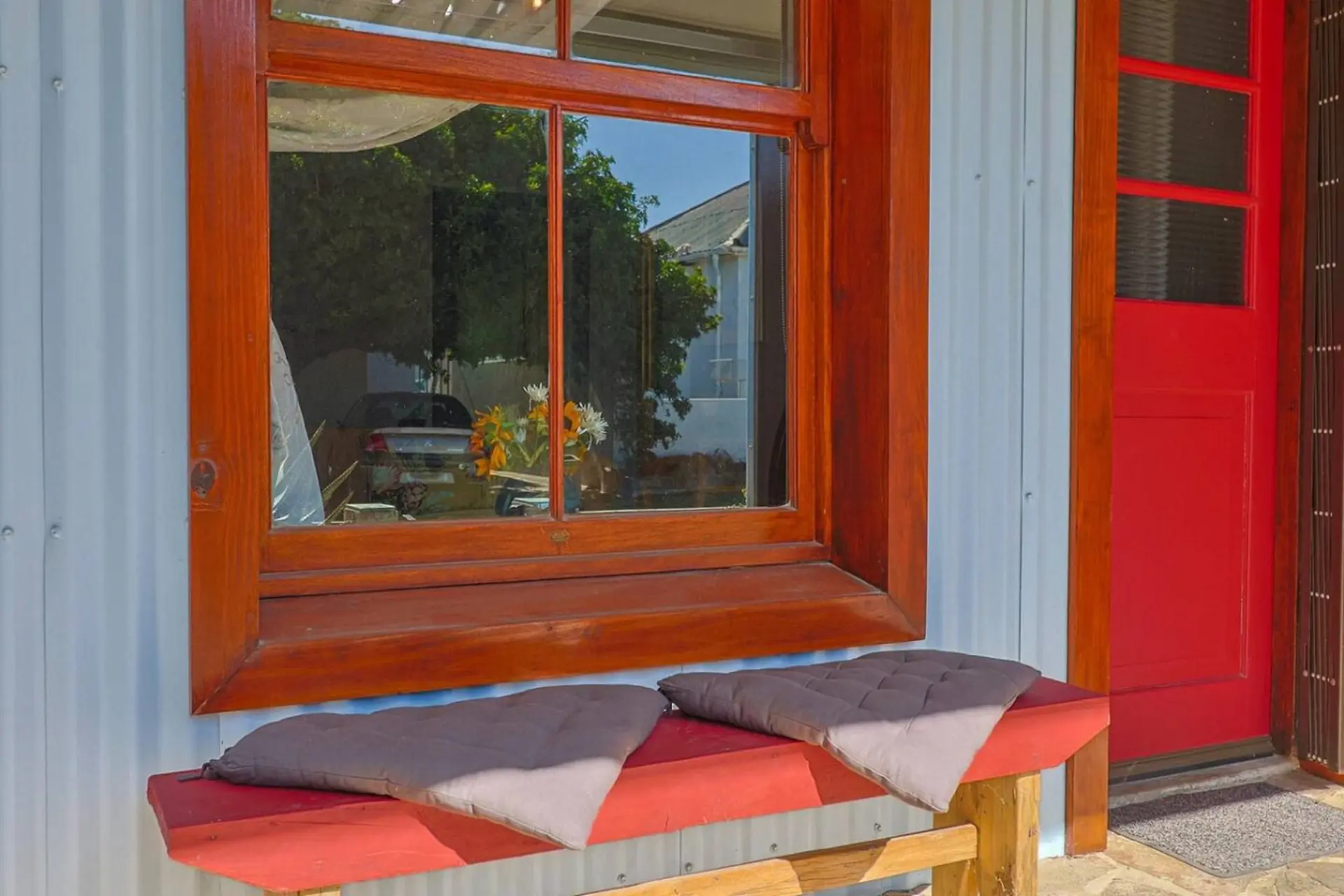 Bench with cushions in front of a window and a red door.