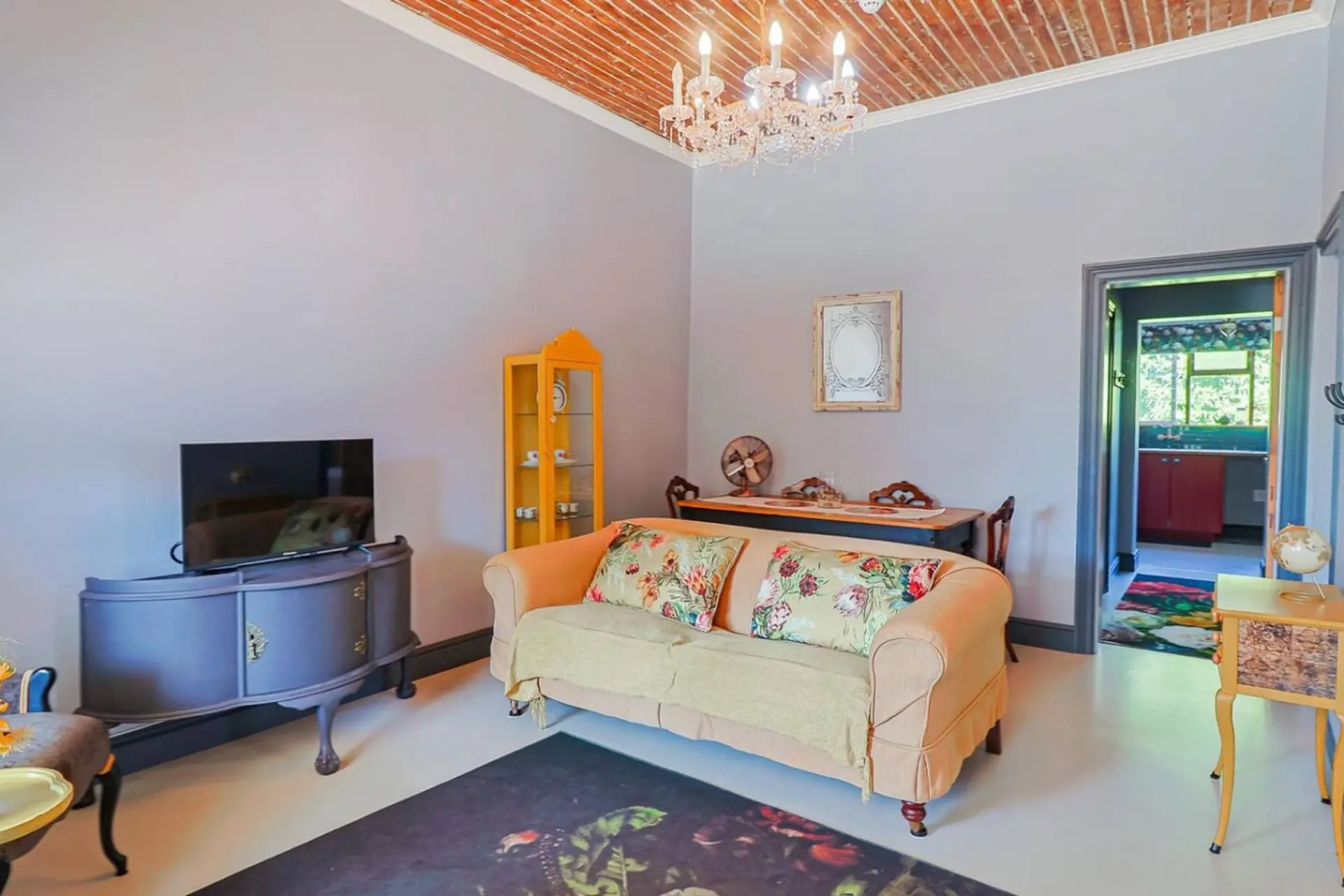 A living room with a sofa, TV, chandelier, and a view into a kitchen.
