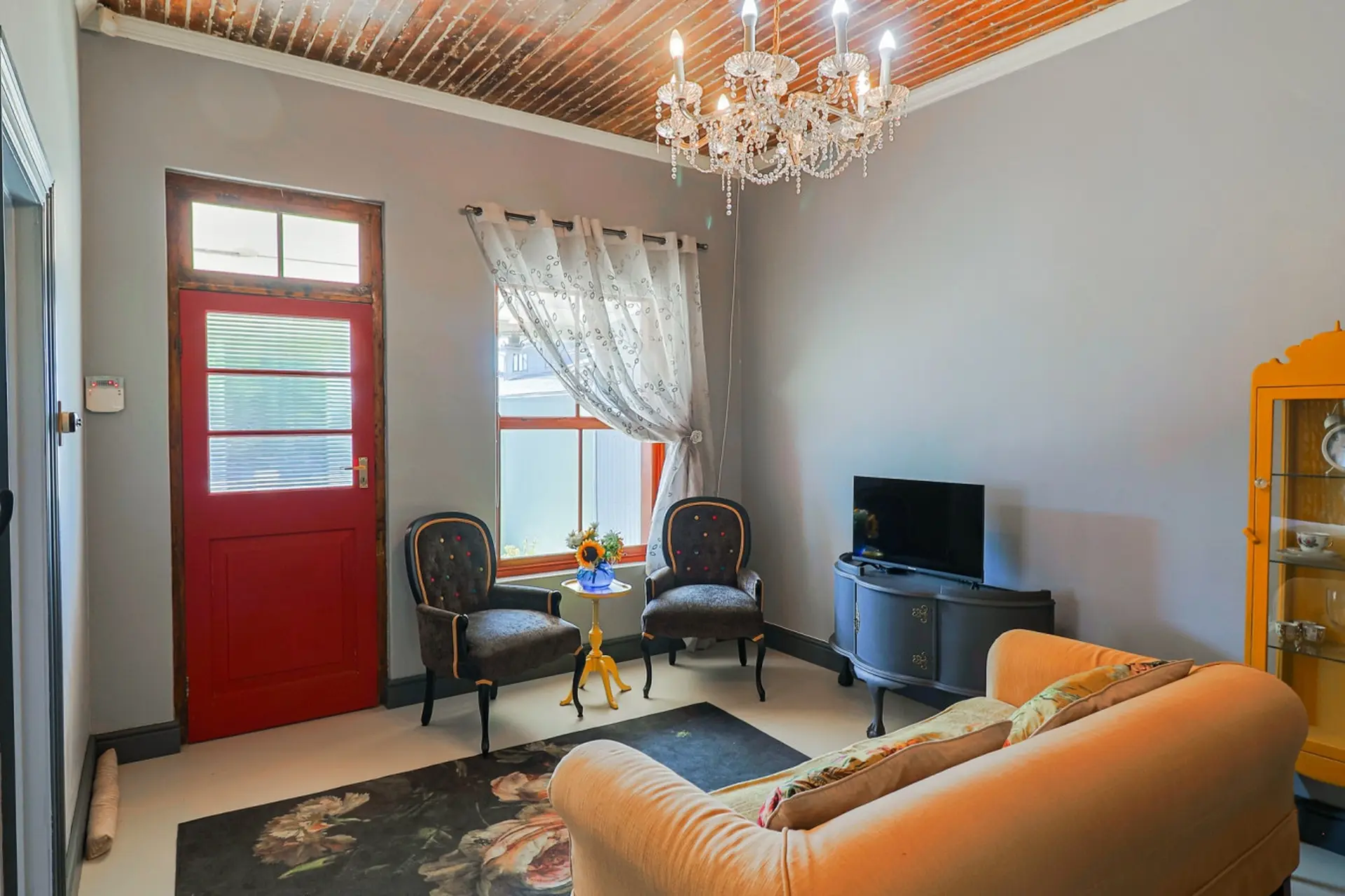 A vintage living room with a red door, ornate chairs, and a crystal chandelier.