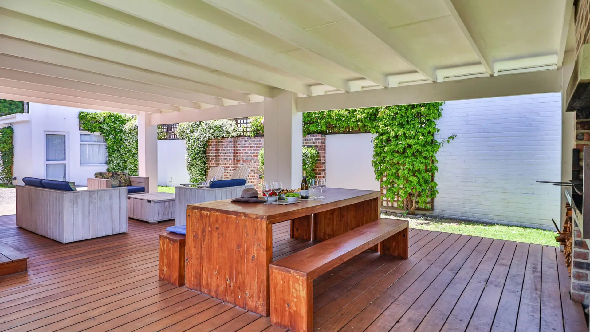 An outdoor patio with a wooden table, benches, sofas, and a grill.