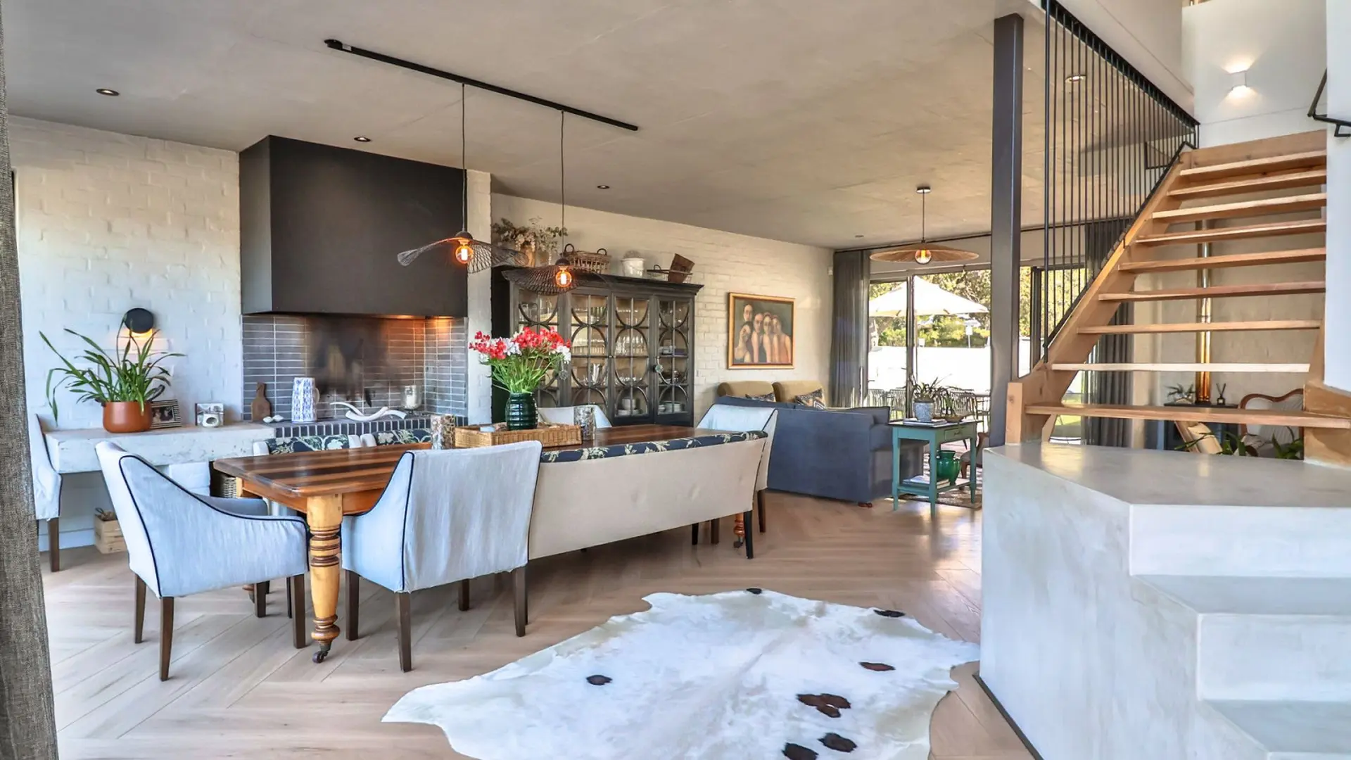 Open-plan dining and living area with fireplace, wooden table, and cowhide rug.