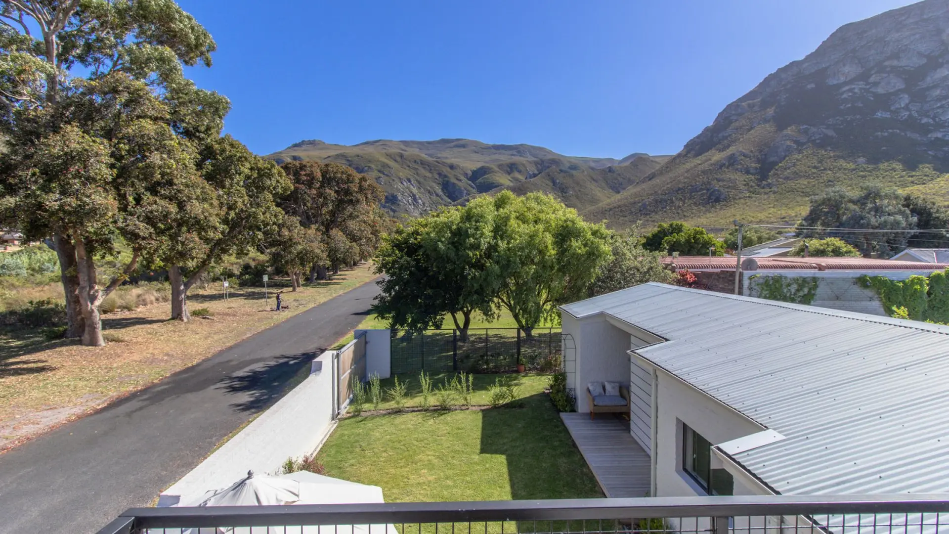 Modern white house with a metal roof overlooking a sunny yard, trees, and mountains.