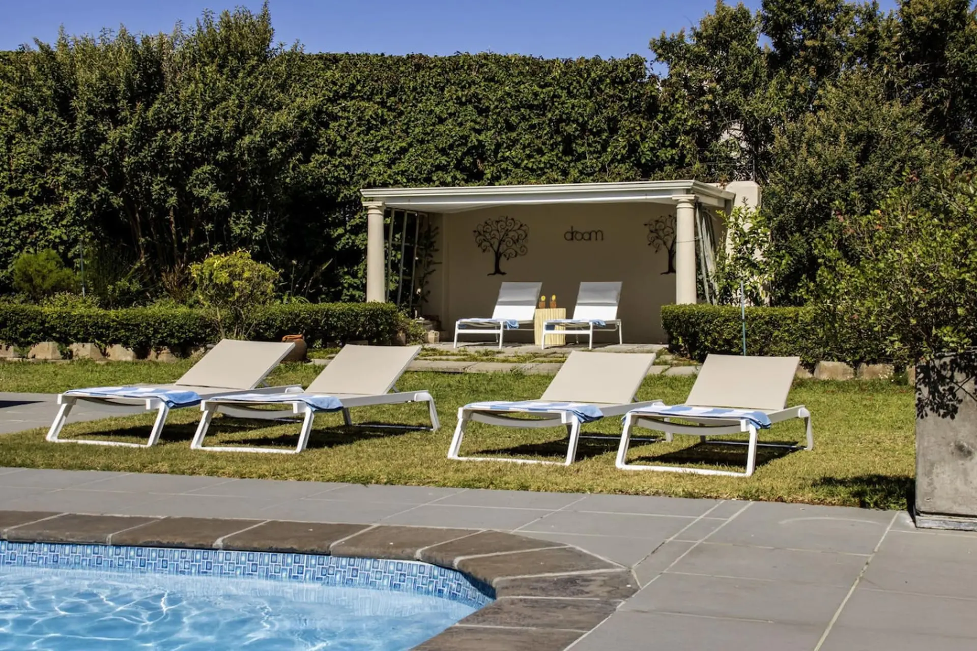 Lounge chairs with blue and white towels beside a pool with a hedge background.