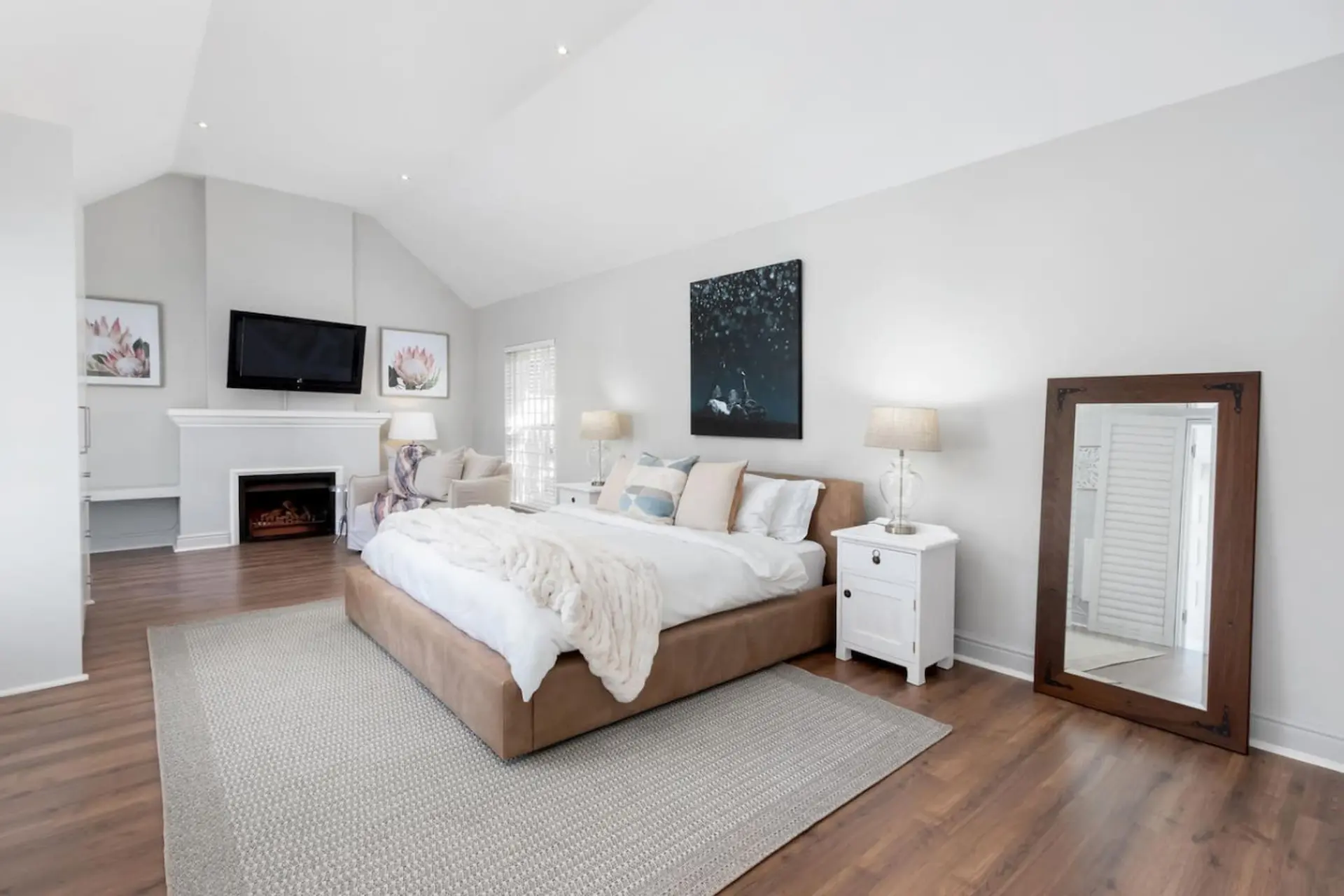 A spacious bedroom with a king-size bed, fireplace, TV, and a large mirror.