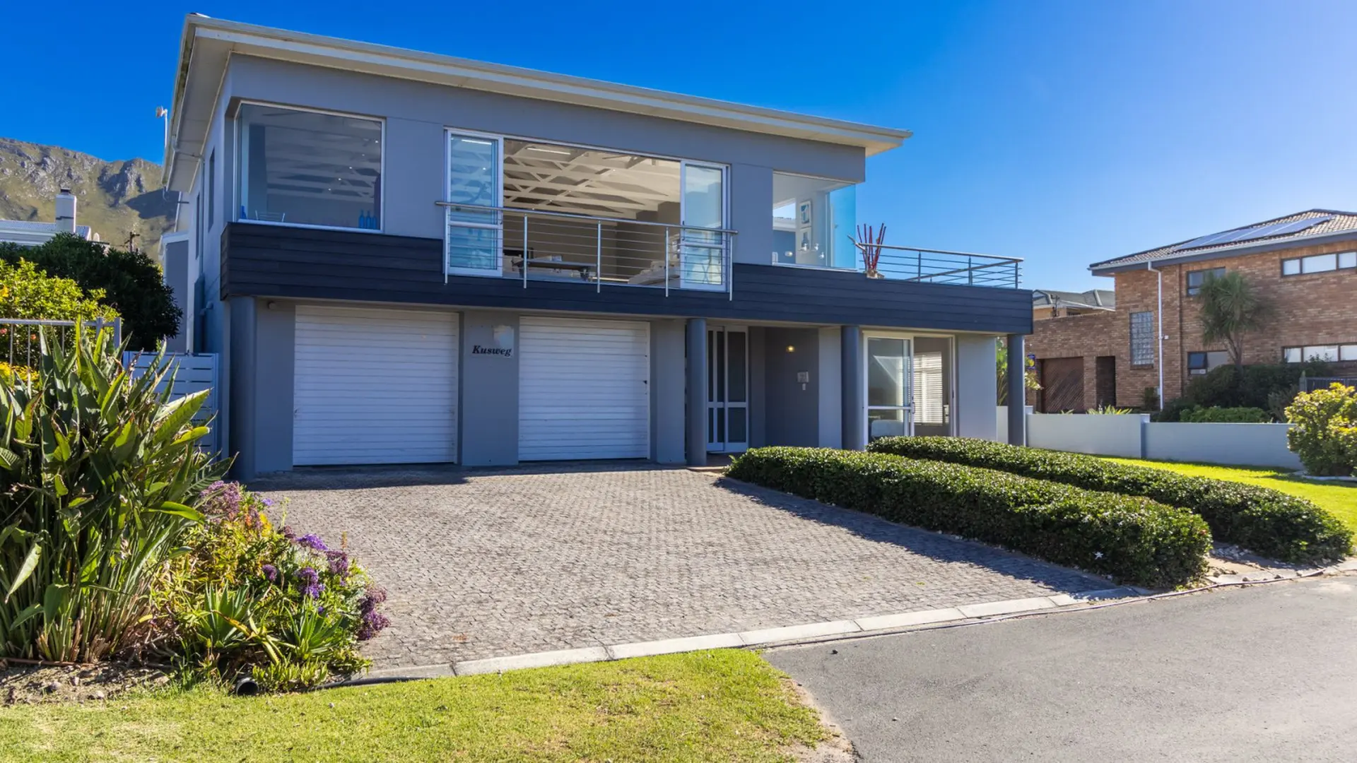 A modern grey house with a double garage, a balcony, and a well-manicured garden.