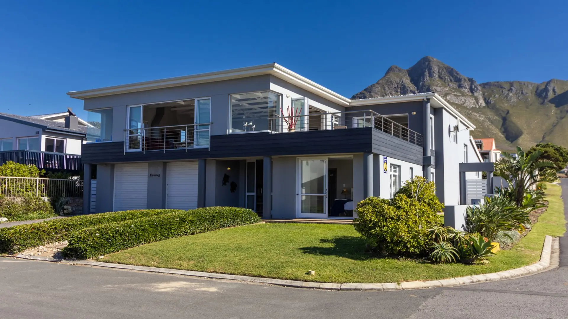 Modern gray house with balconies and large windows, against a backdrop of mountains.