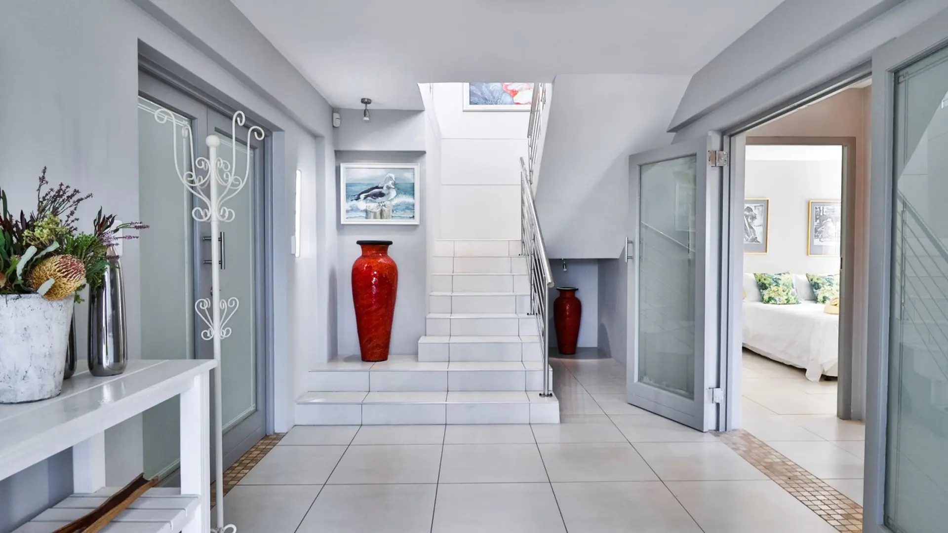 A hallway with a staircase, two red vases, and a bedroom.
