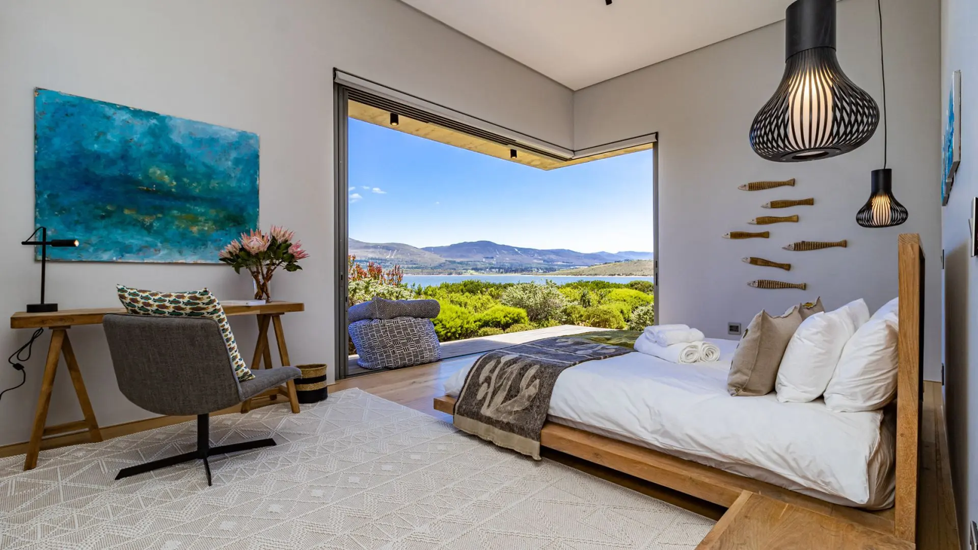 Bedroom with a large window overlooking a lake and mountains.