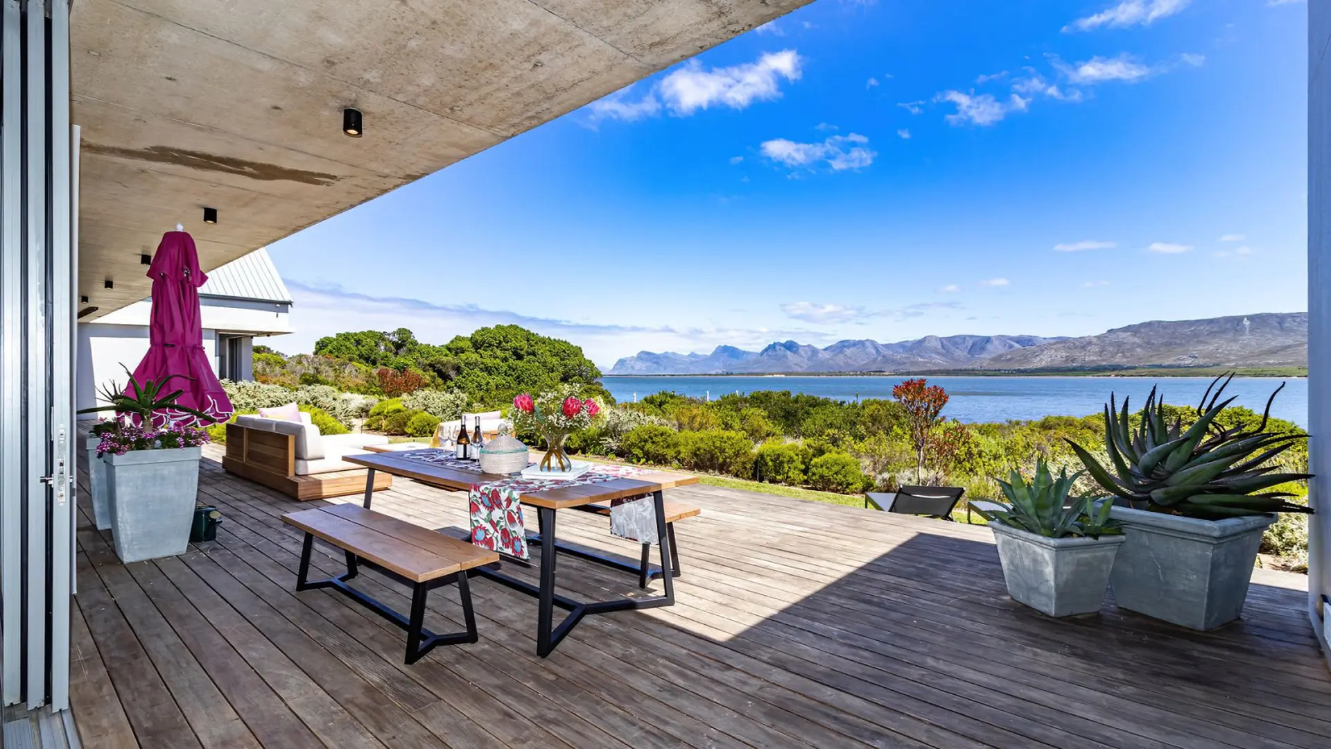 A covered patio with a wooden deck overlooking a bay and mountains.